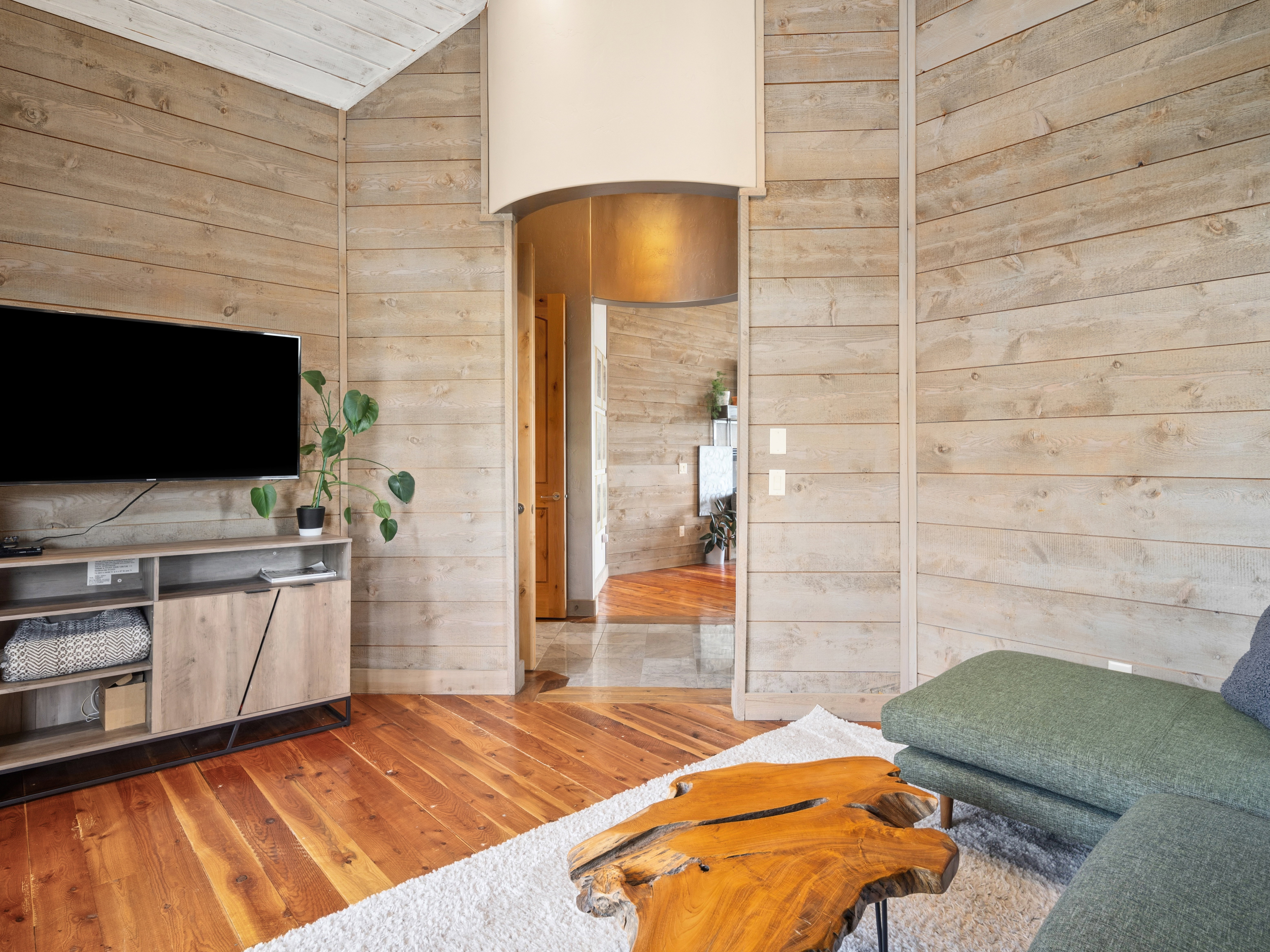 Living area featuring warm wood-finish flooring, horizontal wood paneling, and an arched entryway