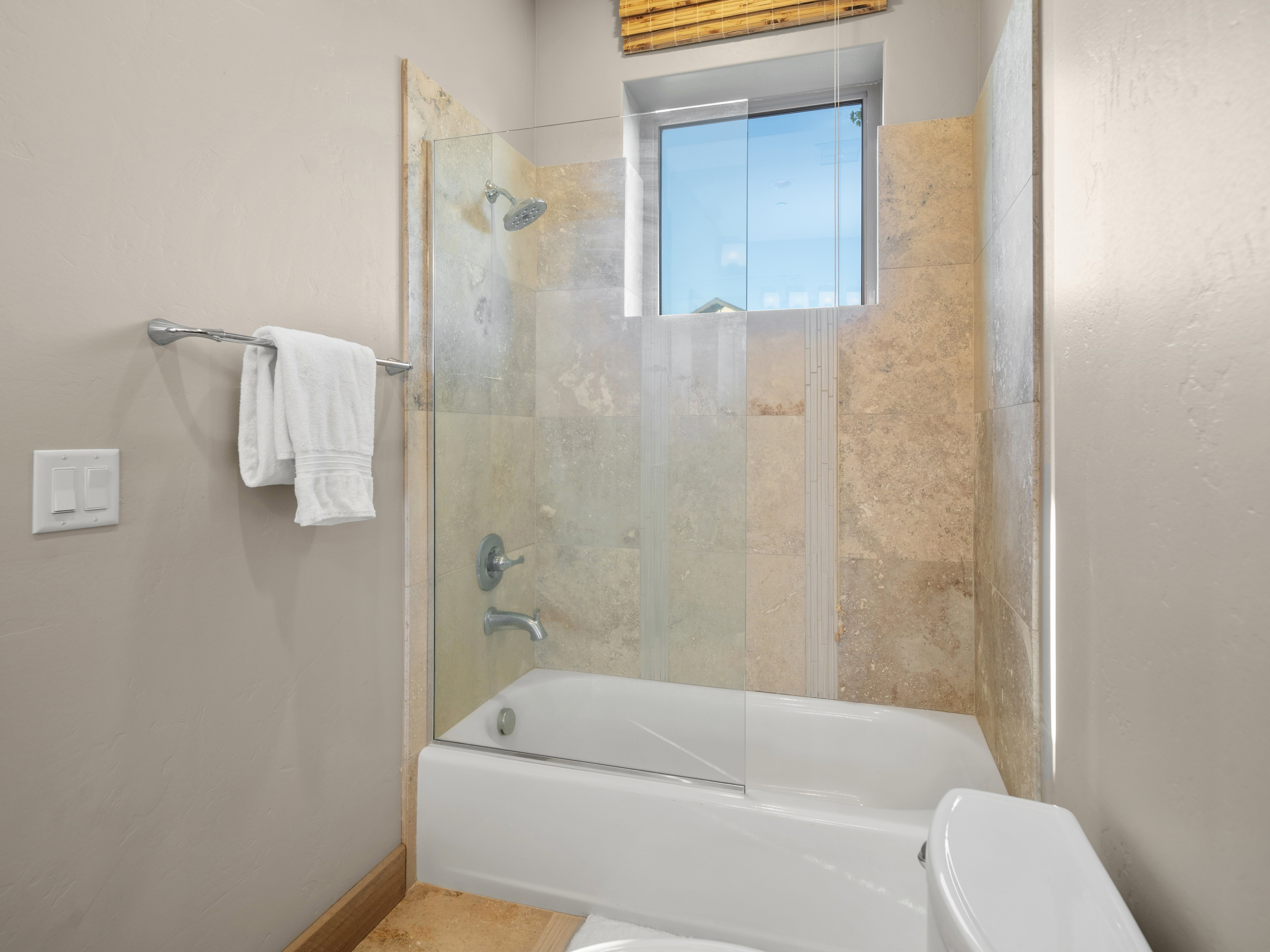 Bathroom featuring a white tub, glass shower enclosure, and stone-look tile surround