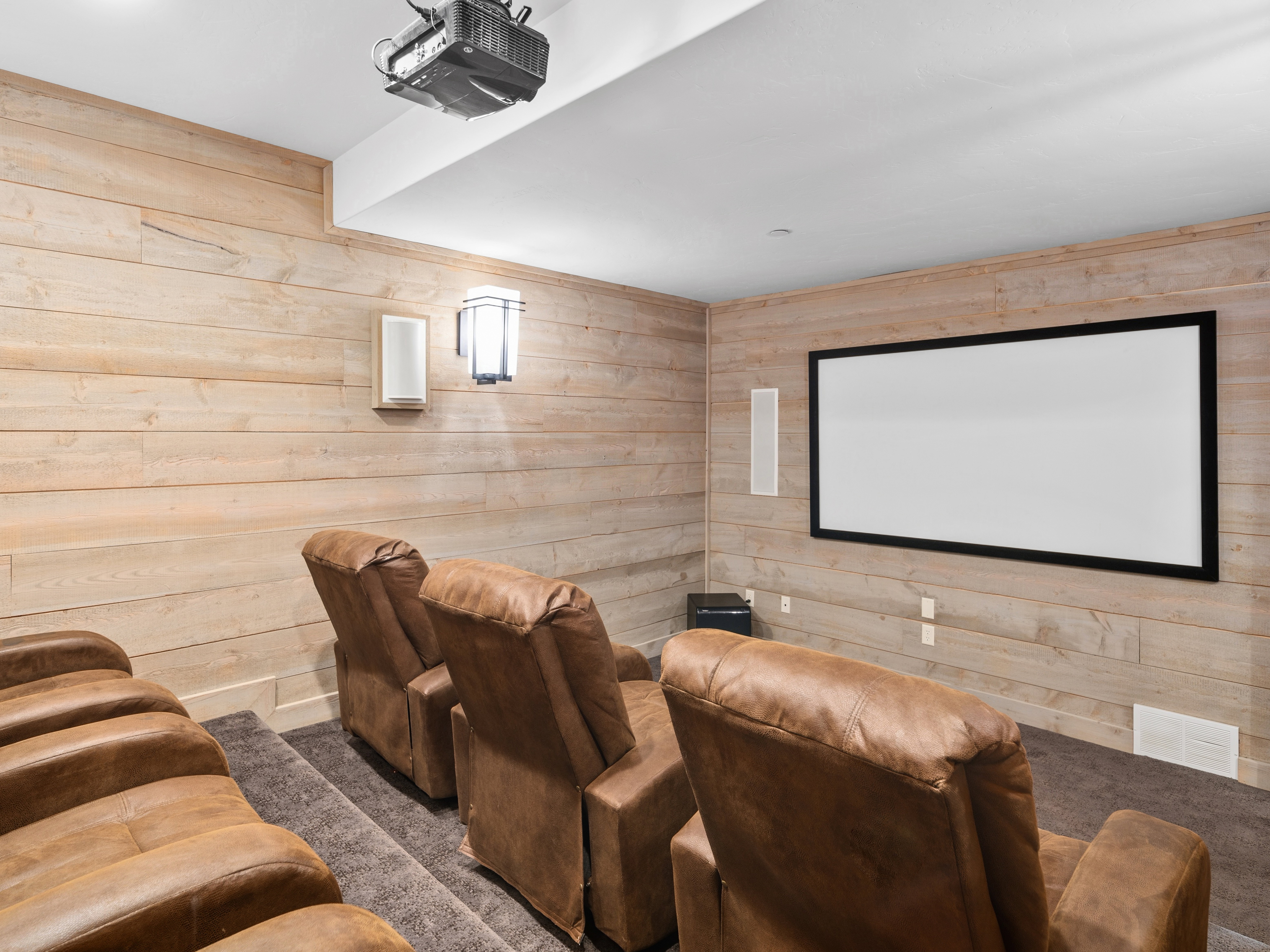 Dedicated home theater featuring tiered seating, a large projection screen, a ceiling-mounted projector, wood-paneled walls, and integrated wall speakers
