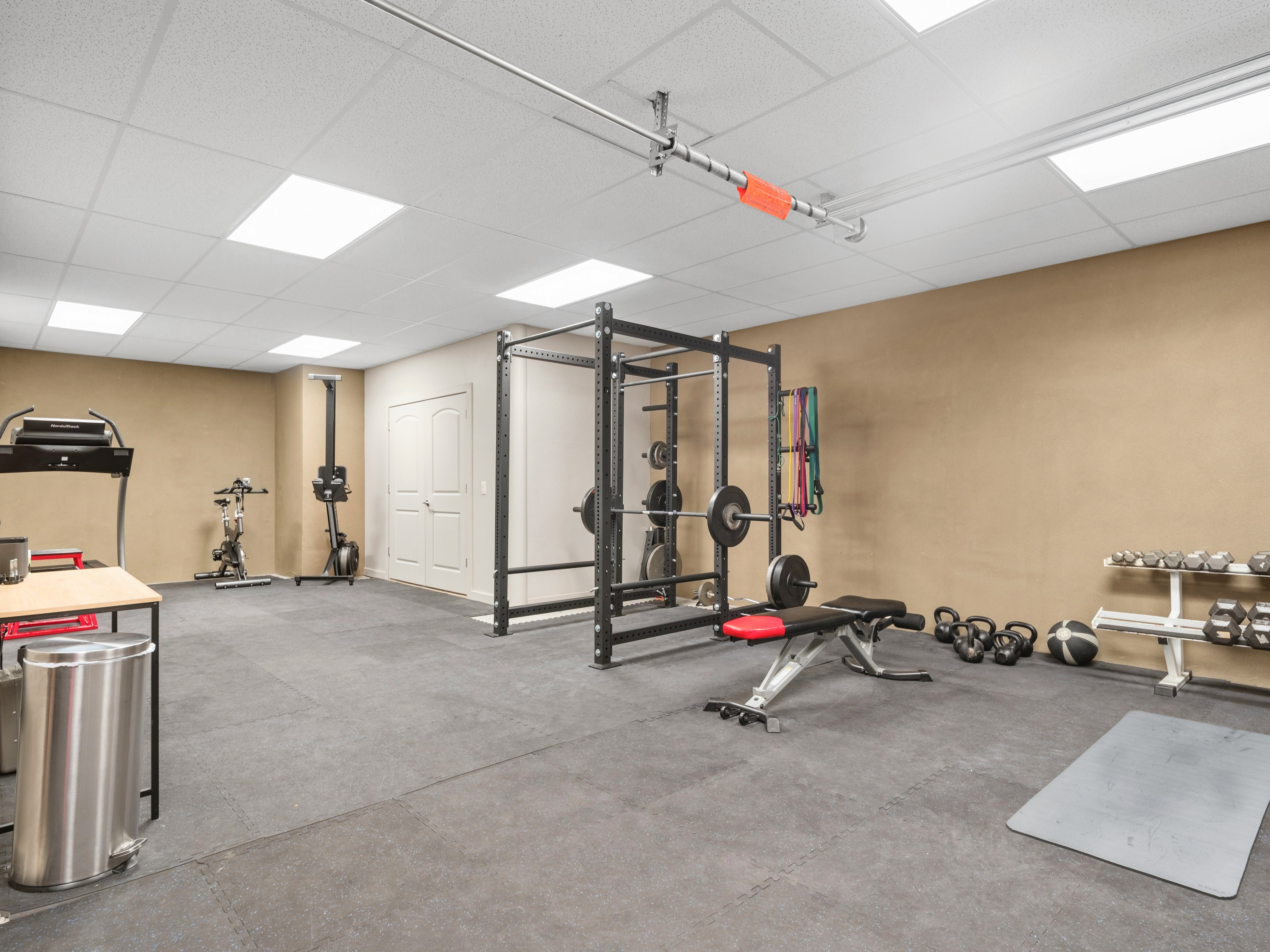 Spacious room featuring durable rubber flooring, neutral wall tones, and a drop ceiling with integrated rectangular lighting fixtures