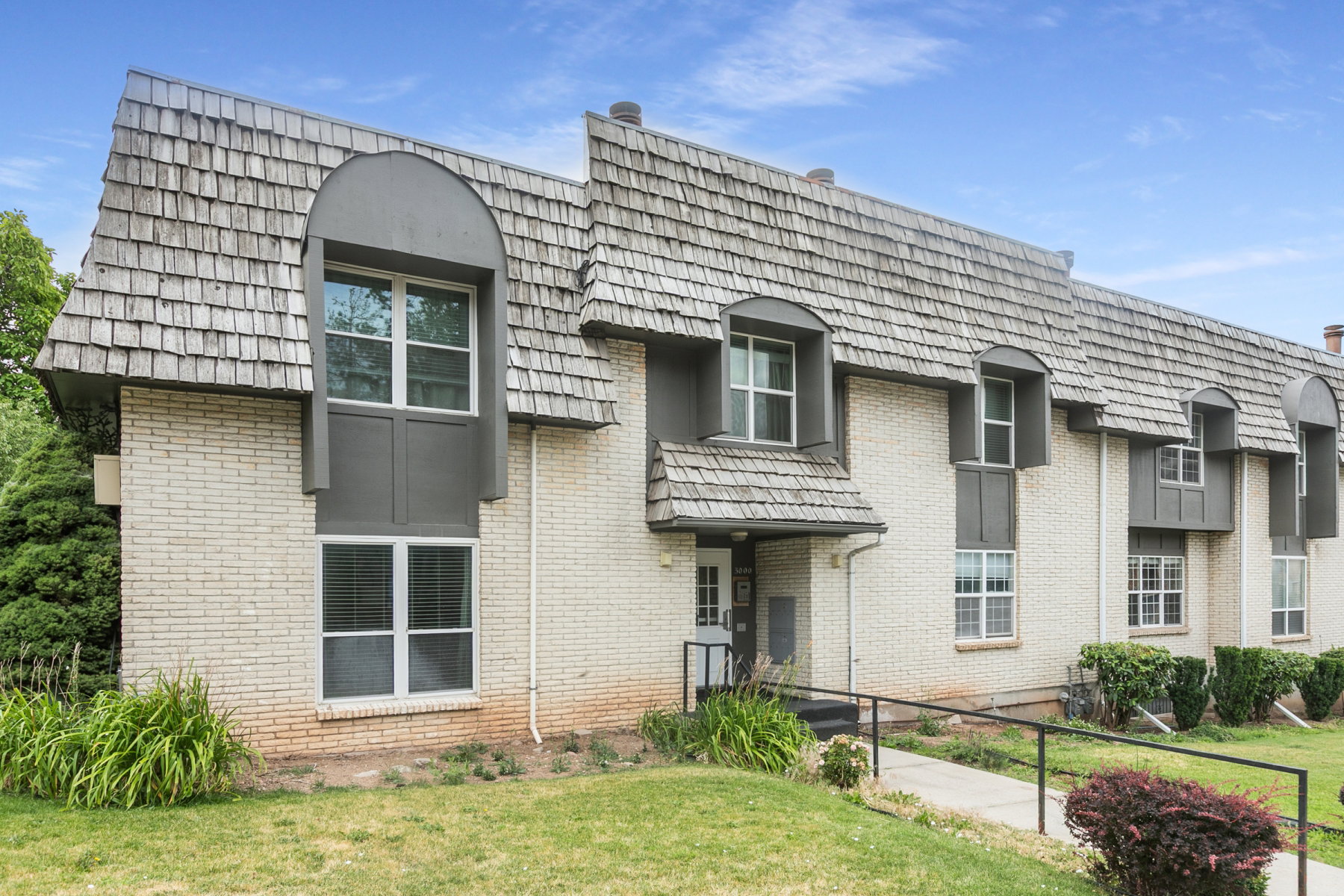 Multi-story residential building featuring light brick exterior and wood shake roofing