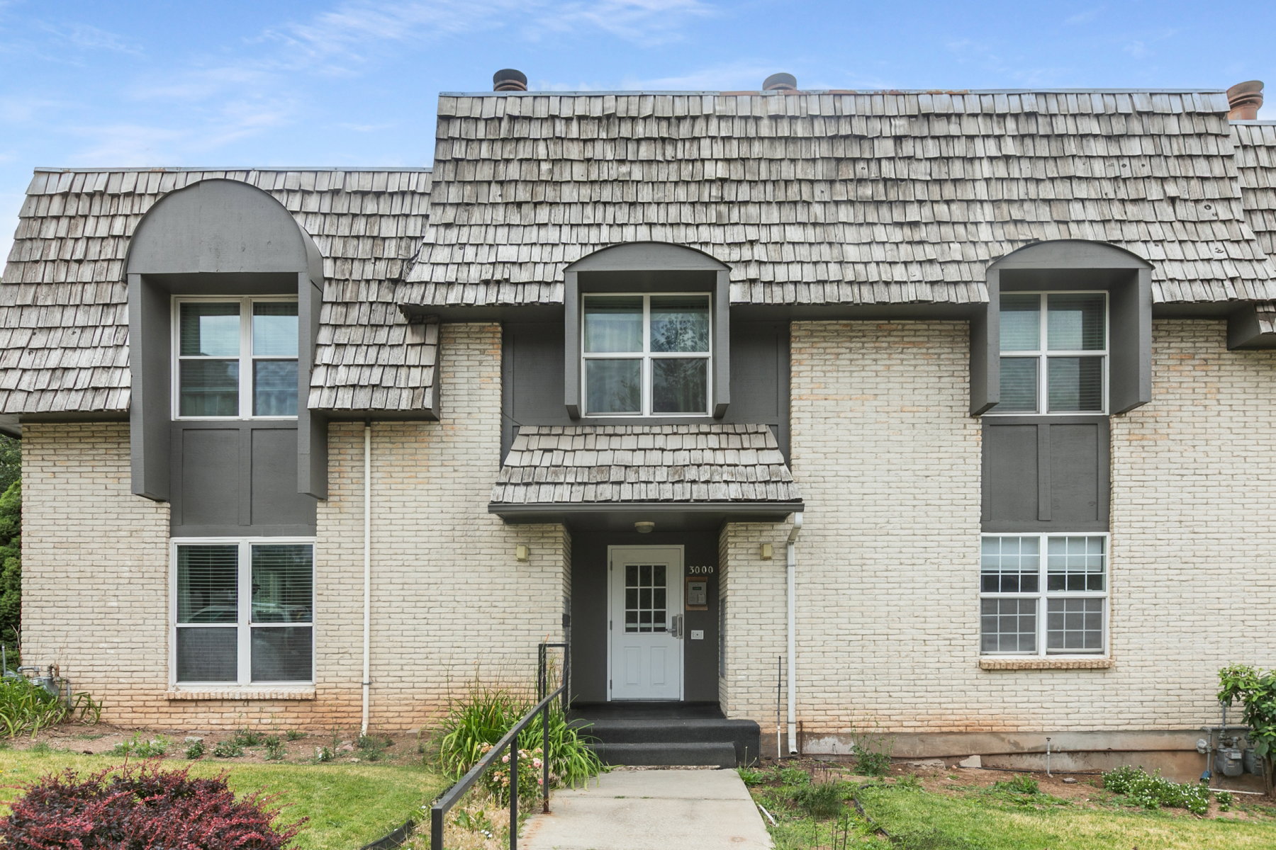 Cream brick exterior featuring a white entry door, black handrail, and gray dormer windows