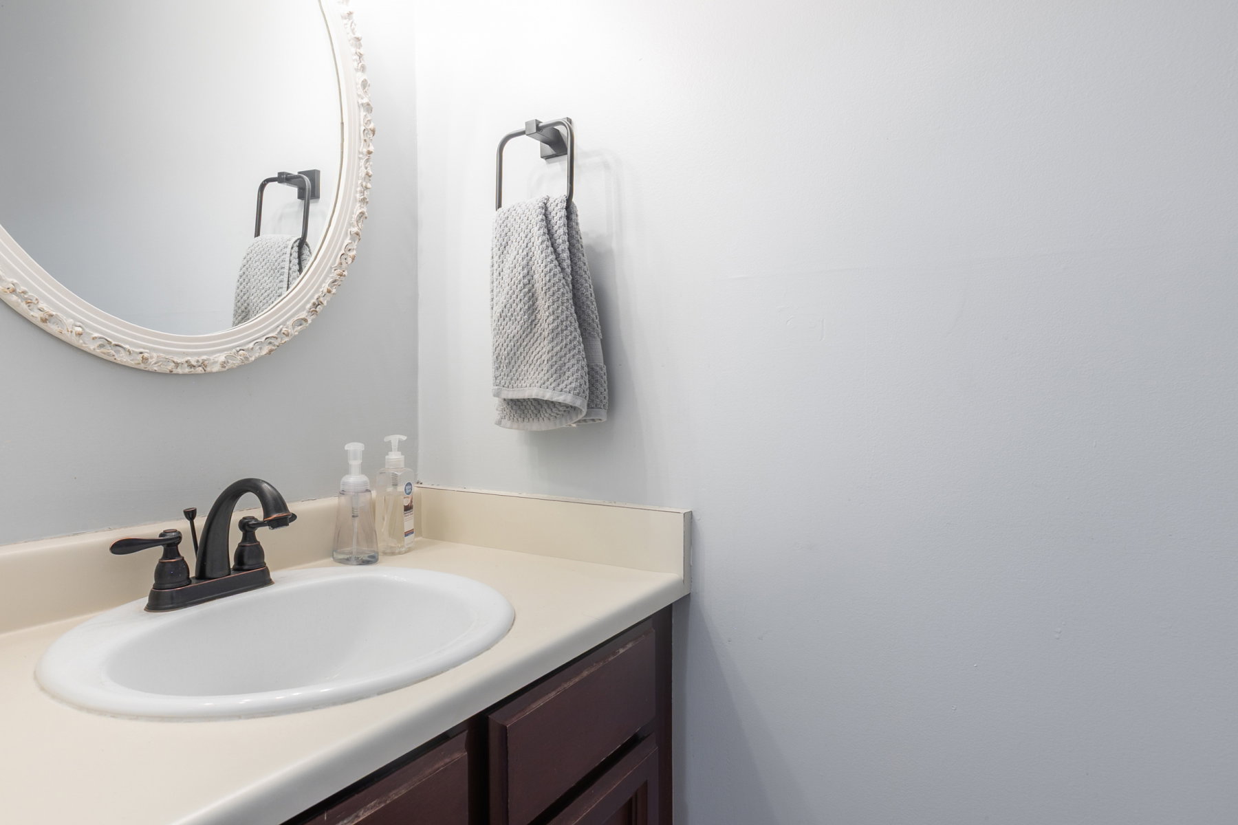 Bathroom vanity featuring an oval undermount sink, oil-rubbed bronze faucet, beige countertop, and dark wood-finish cabinetry