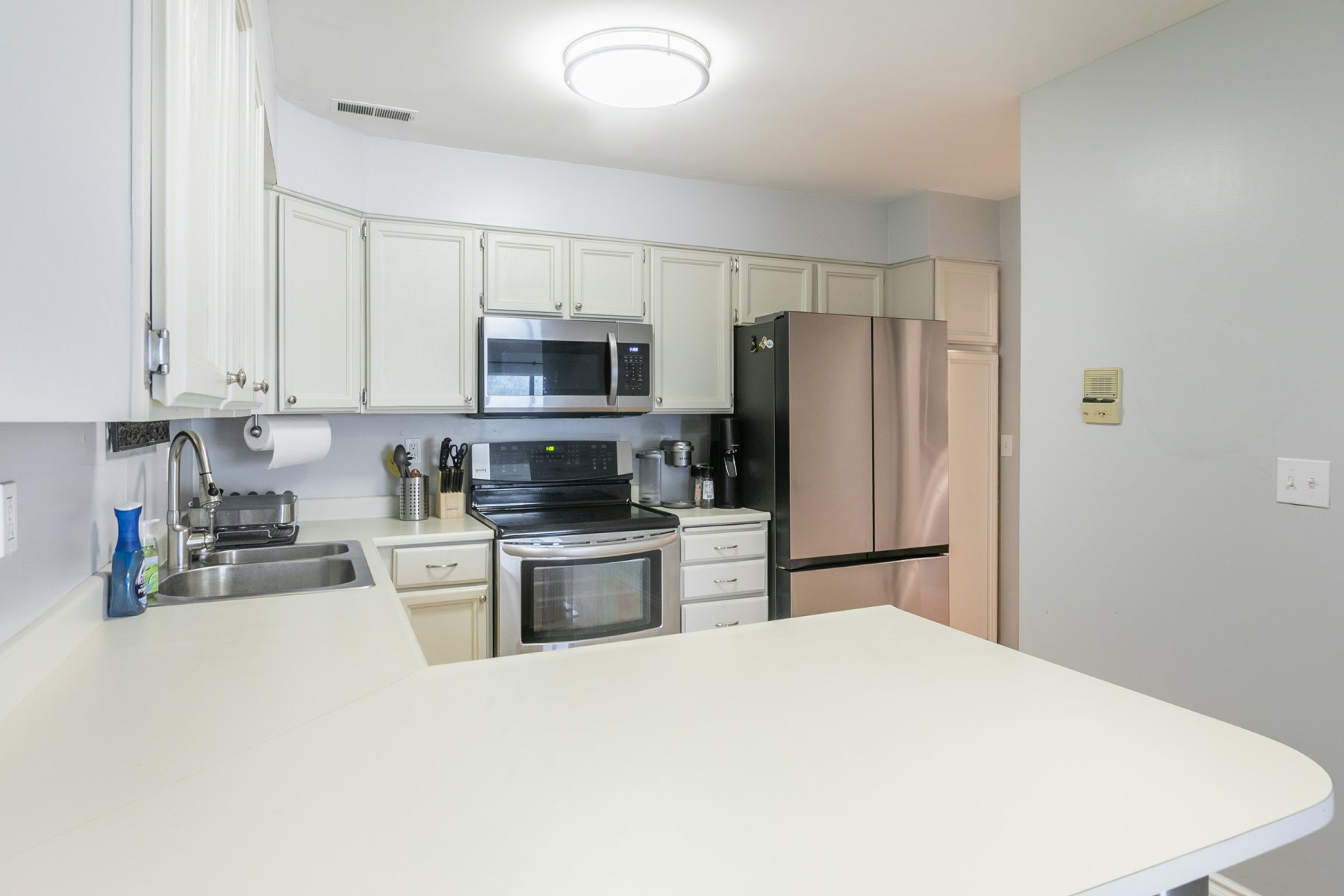 Kitchen featuring white cabinetry with silver hardware, white countertops, stainless steel appliances, and a double basin sink