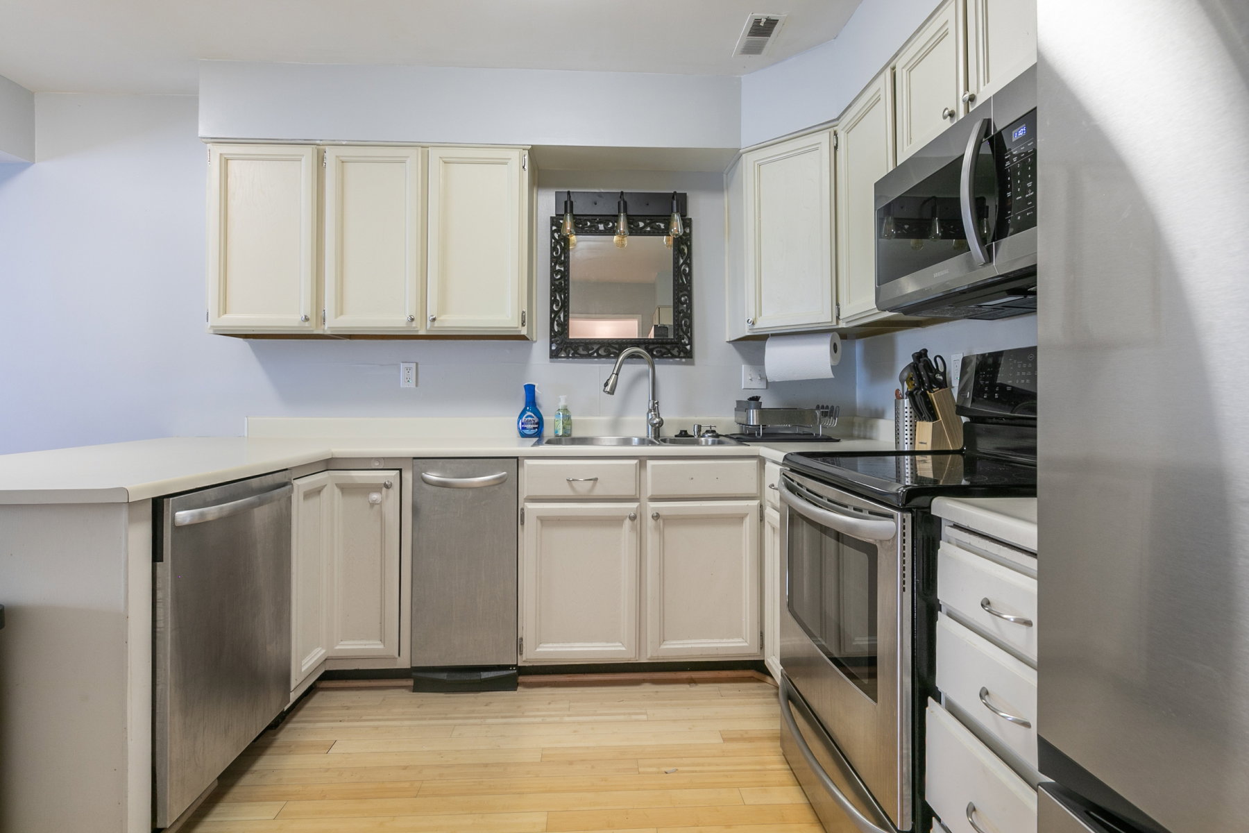 Kitchen featuring light wood-finish flooring, white cabinetry, light countertops, and stainless steel appliances including a dishwasher, range, and built-in microwave