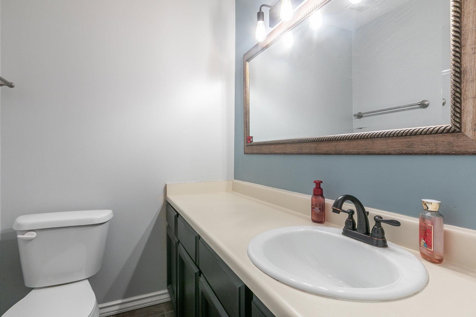 Bathroom vanity with an oval undermount sink, dark bronze faucet, and a light-toned countertop
