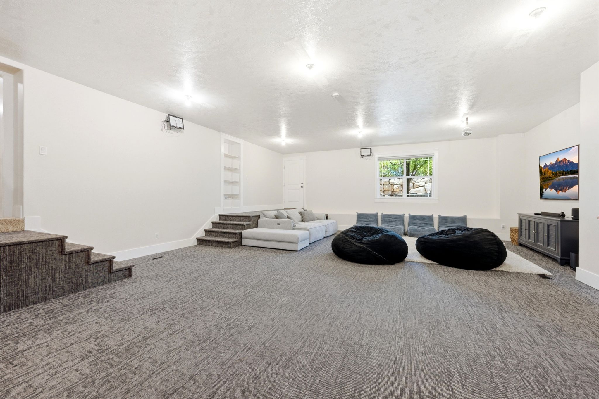 Lower-level entertainment space featuring textured carpeting, recessed lighting, and a built-in shelving unit