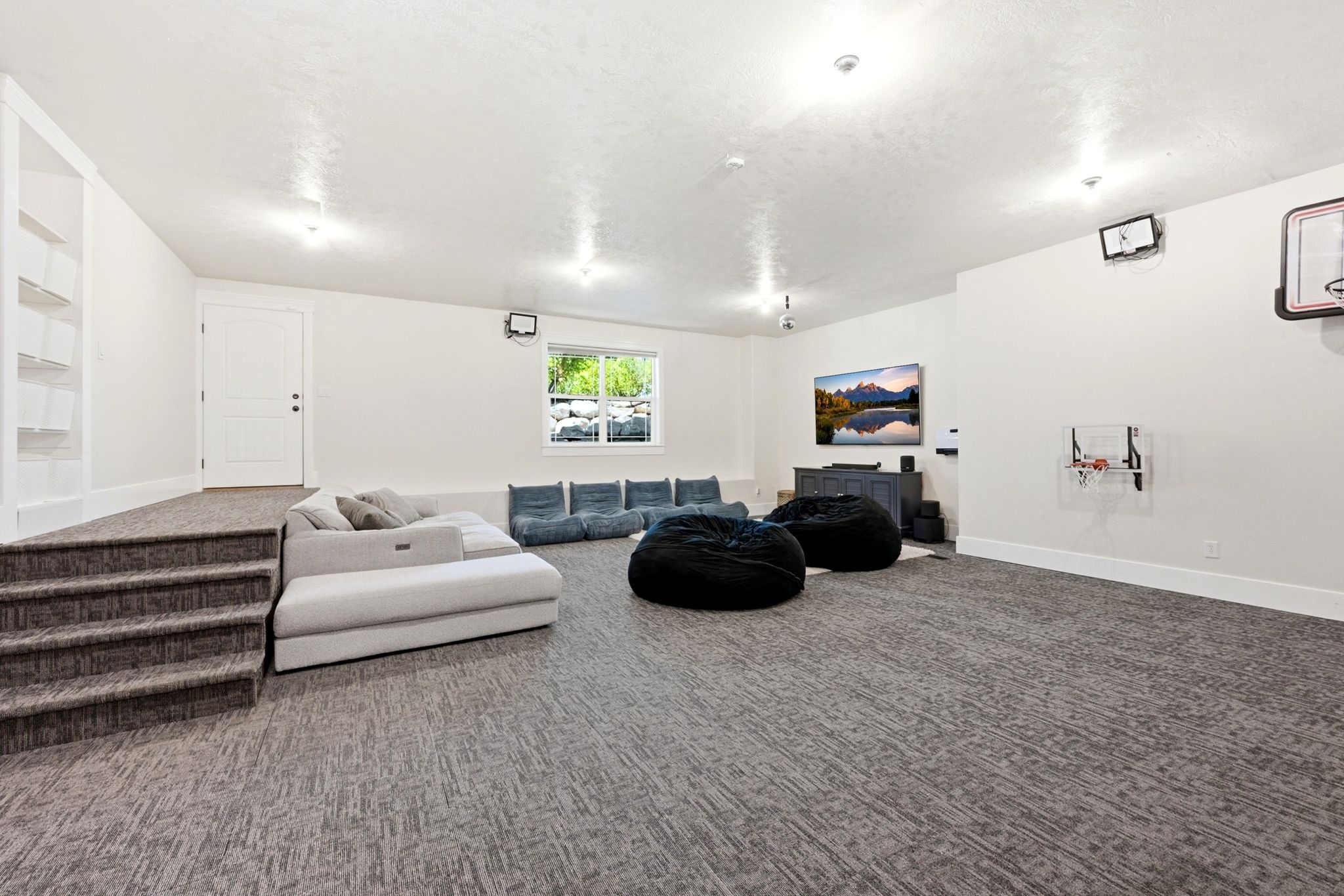 Spacious lower-level room featuring light-toned walls and patterned gray carpeting throughout