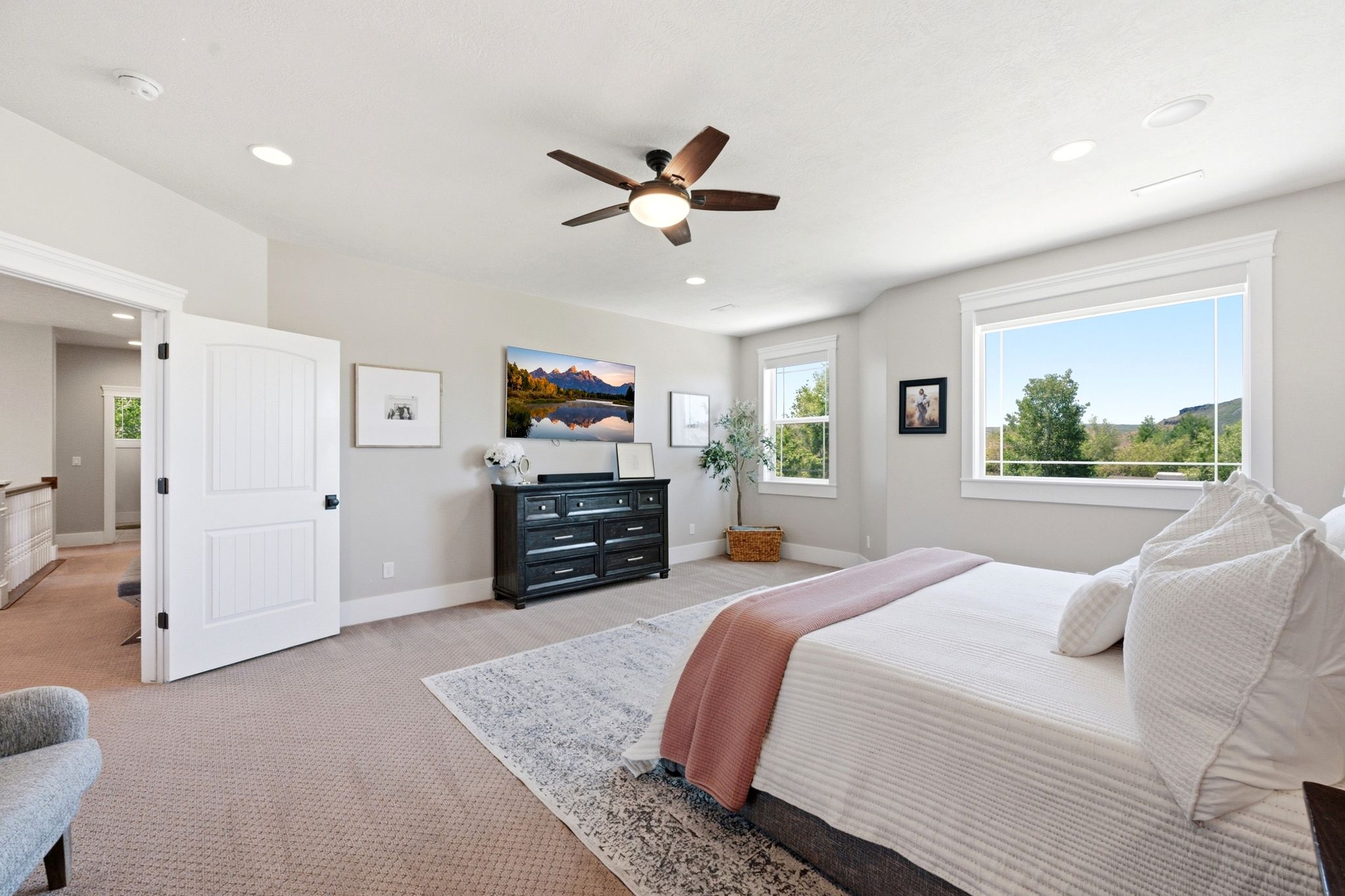 Spacious room featuring neutral carpeting, a dark wood-finish ceiling fan, multiple windows with white trim, and recessed lighting