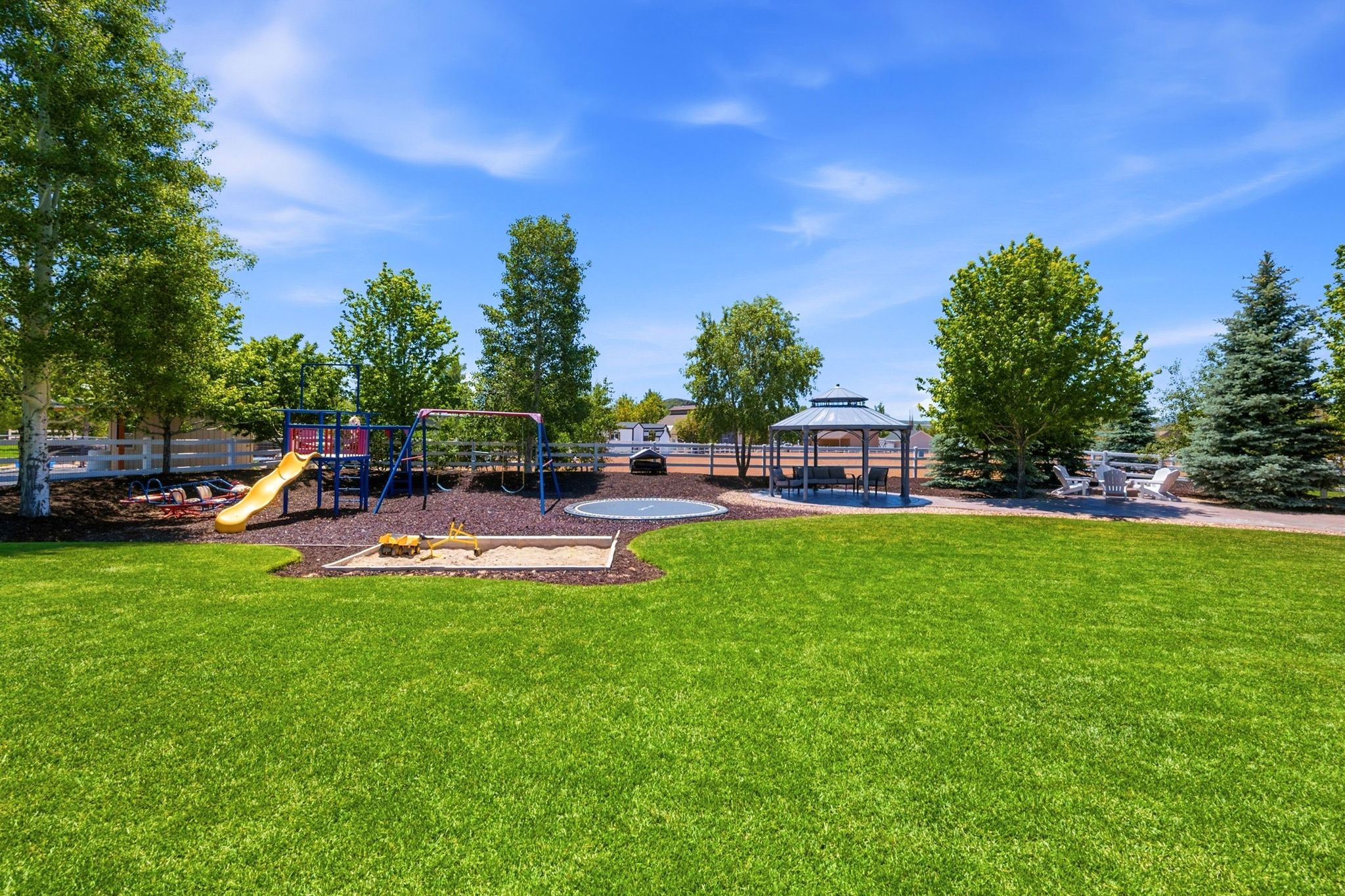 Expansive green lawn area featuring a dedicated playground with slide and swings, a sandbox, and an in-ground trampoline