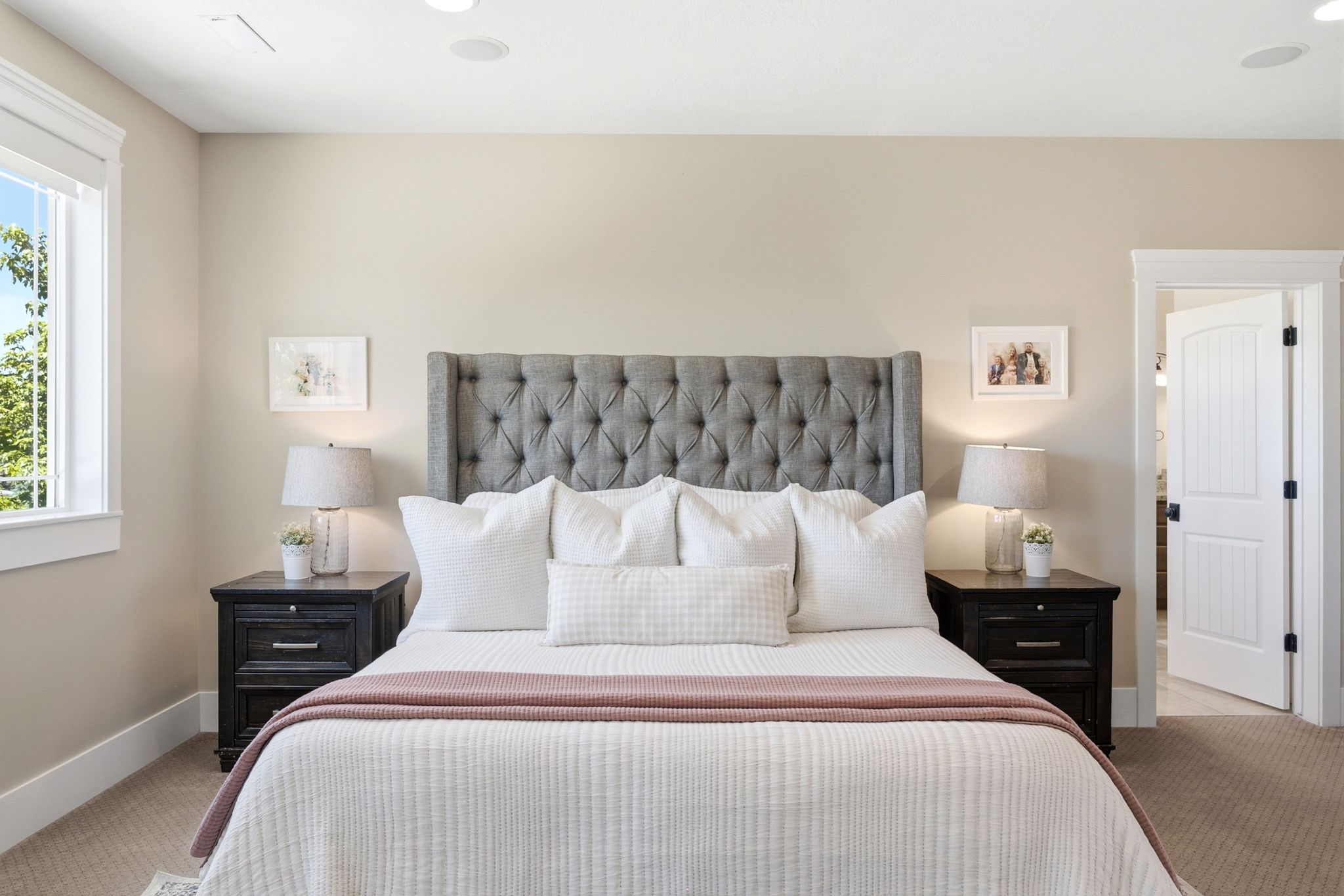 Expansive bedroom featuring a tufted fabric headboard, recessed lighting, a white framed window, and a paneled interior door with dark hardware
