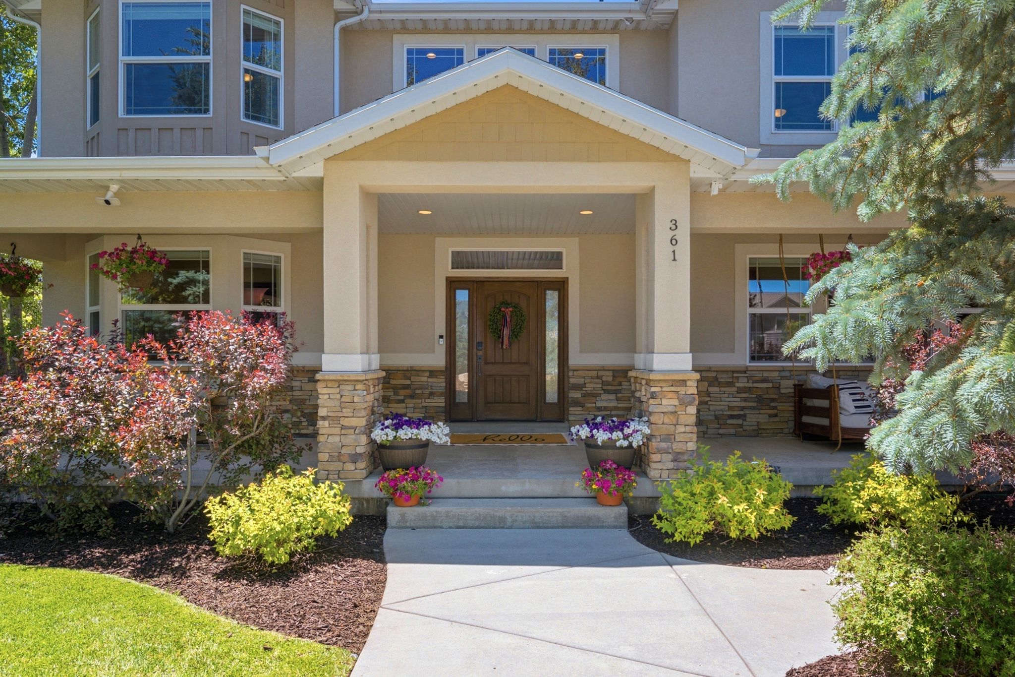 Inviting entryway featuring a covered porch, stone veneer accents, wood-paneled front door with sidelights, and mature landscaping