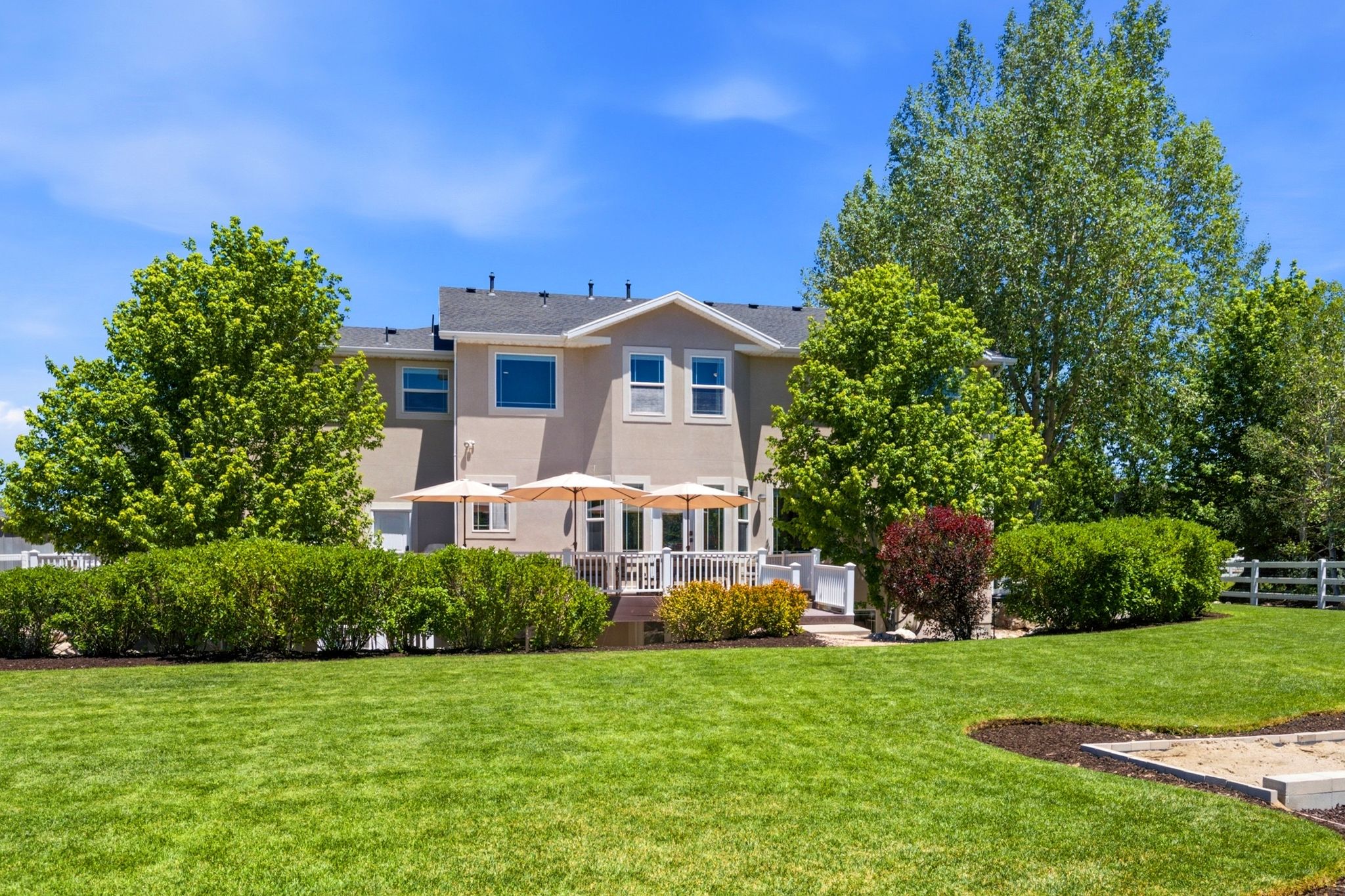 Expansive rear lawn featuring a tiered deck with white railings, mature trees, and established perimeter hedging