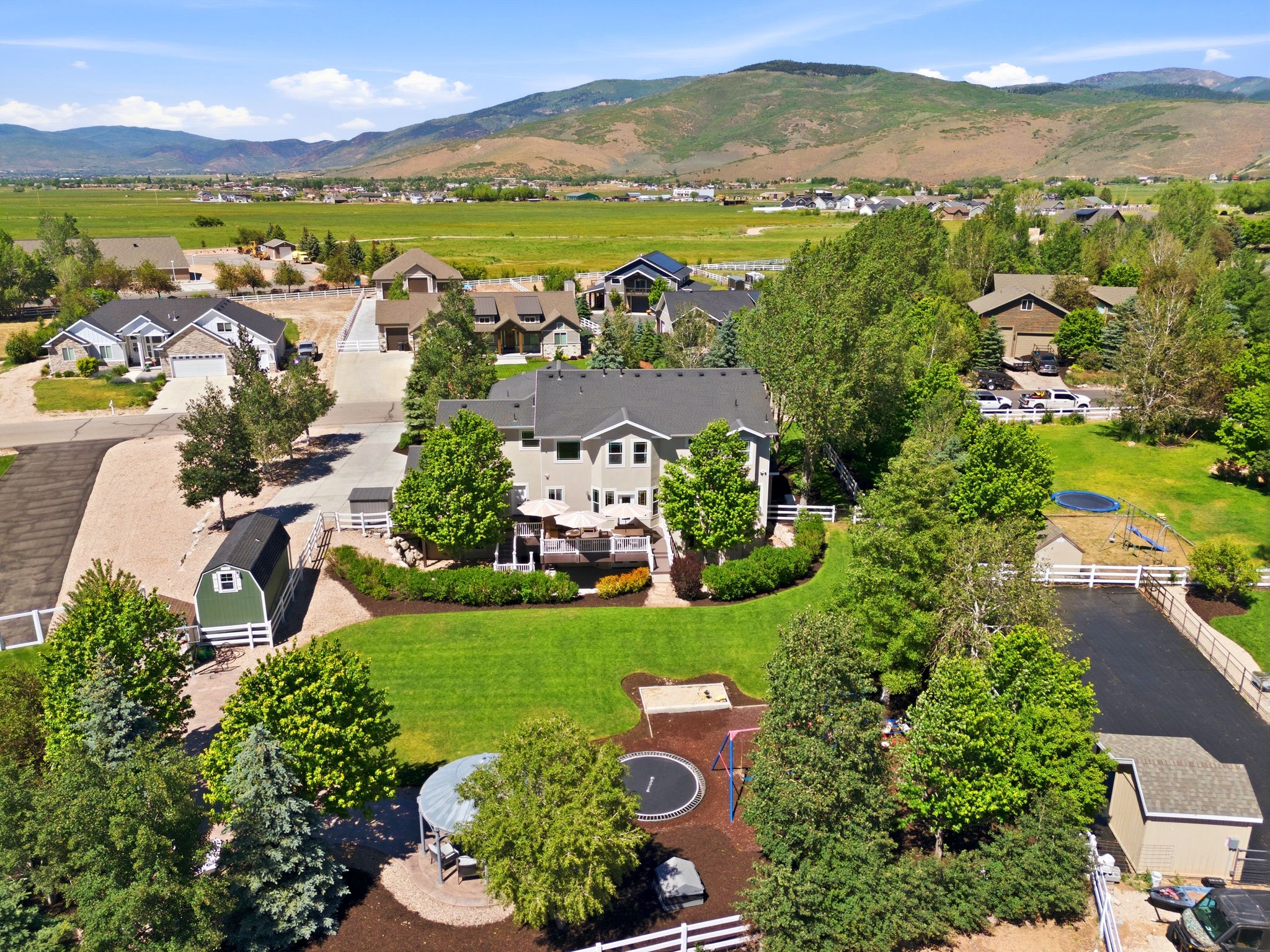 Expansive property featuring a two-story residence with a rear deck, large manicured lawn, established trees, and a detached shed