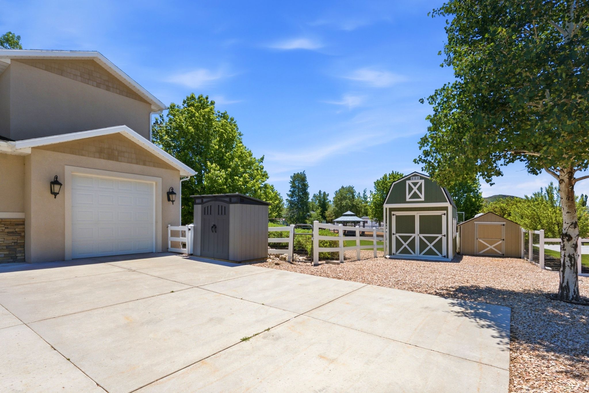 Spacious concrete driveway featuring a two-car garage with sconce lighting, stone accenting, and a gabled entry