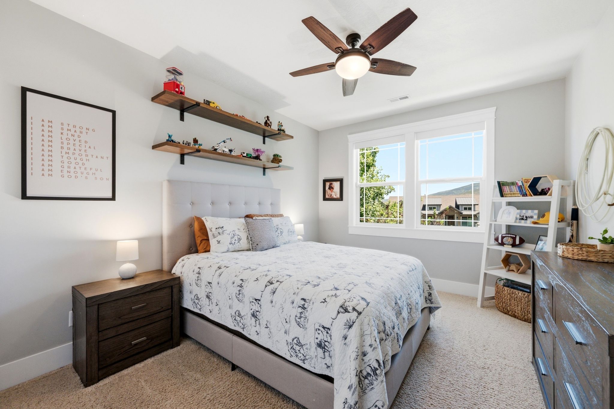 Room featuring a ceiling fan with integrated lighting, wood-finish floating shelves with black brackets, and a tufted headboard