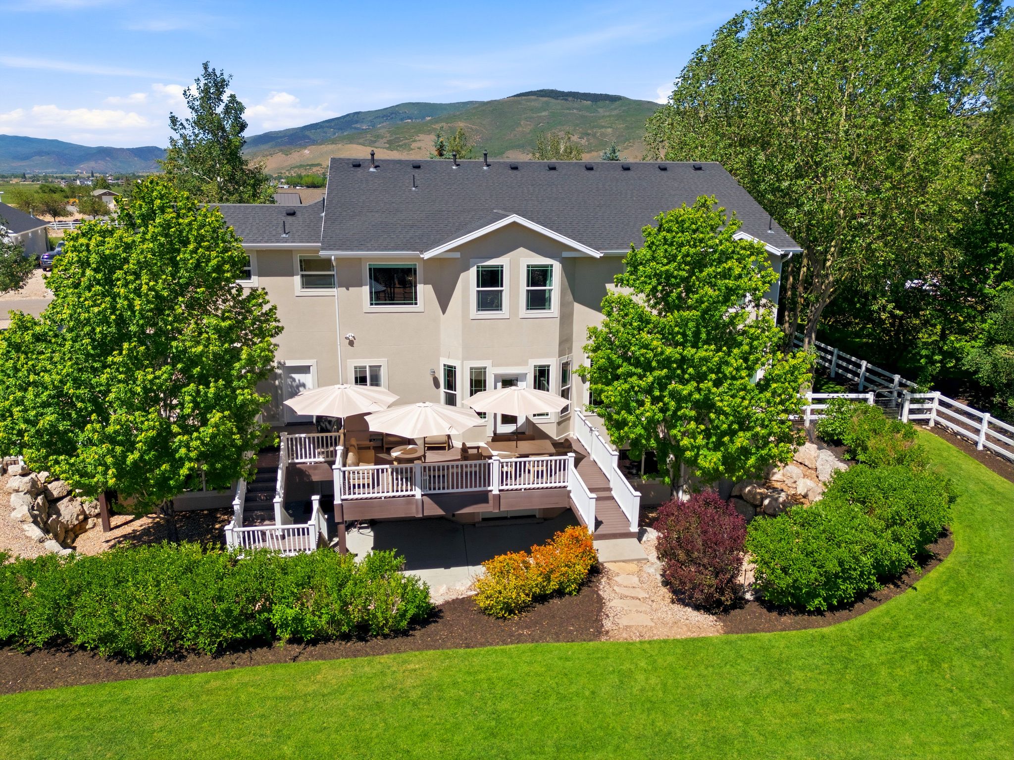 Rear exterior featuring a multi-level deck with white railings, a lower-level patio, and extensive landscaping