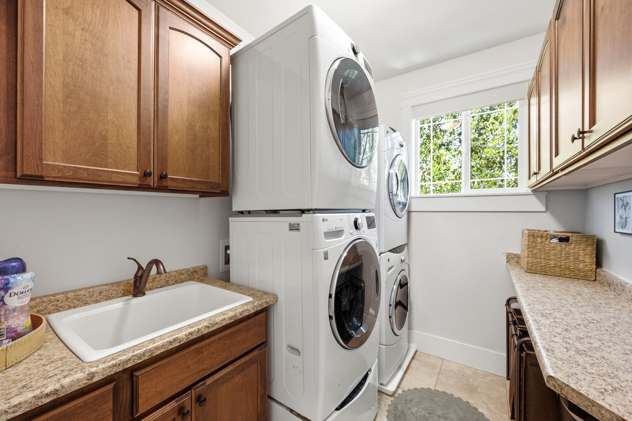 Dedicated laundry room featuring stacked washer and dryer units, a utility sink with a bronze-finish faucet, ample wood cabinetry, and a window providing natural light