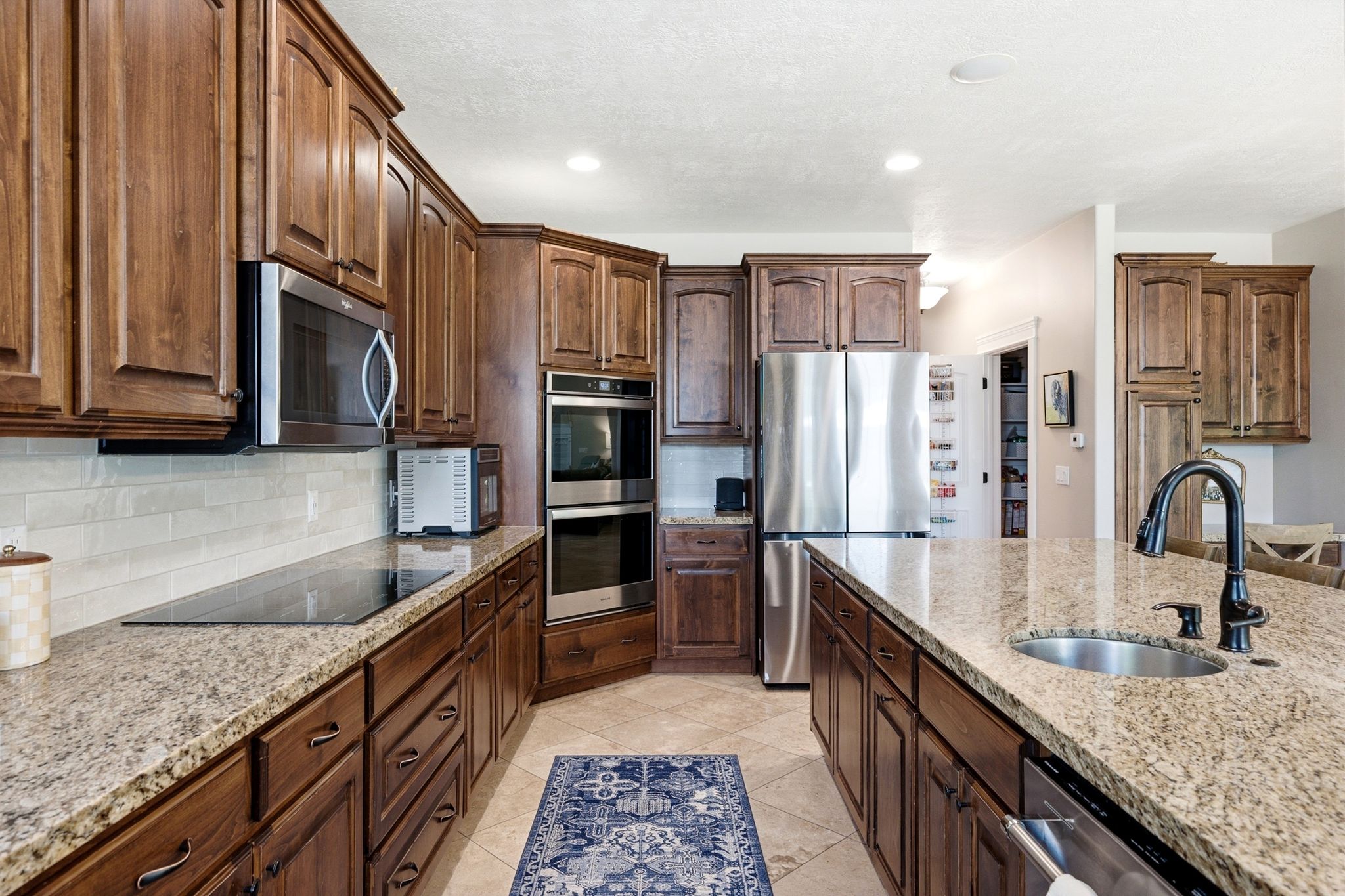Kitchen featuring extensive wood cabinetry, granite countertops, and stainless steel appliances including a built-in microwave, double wall ovens, and a refrigerator