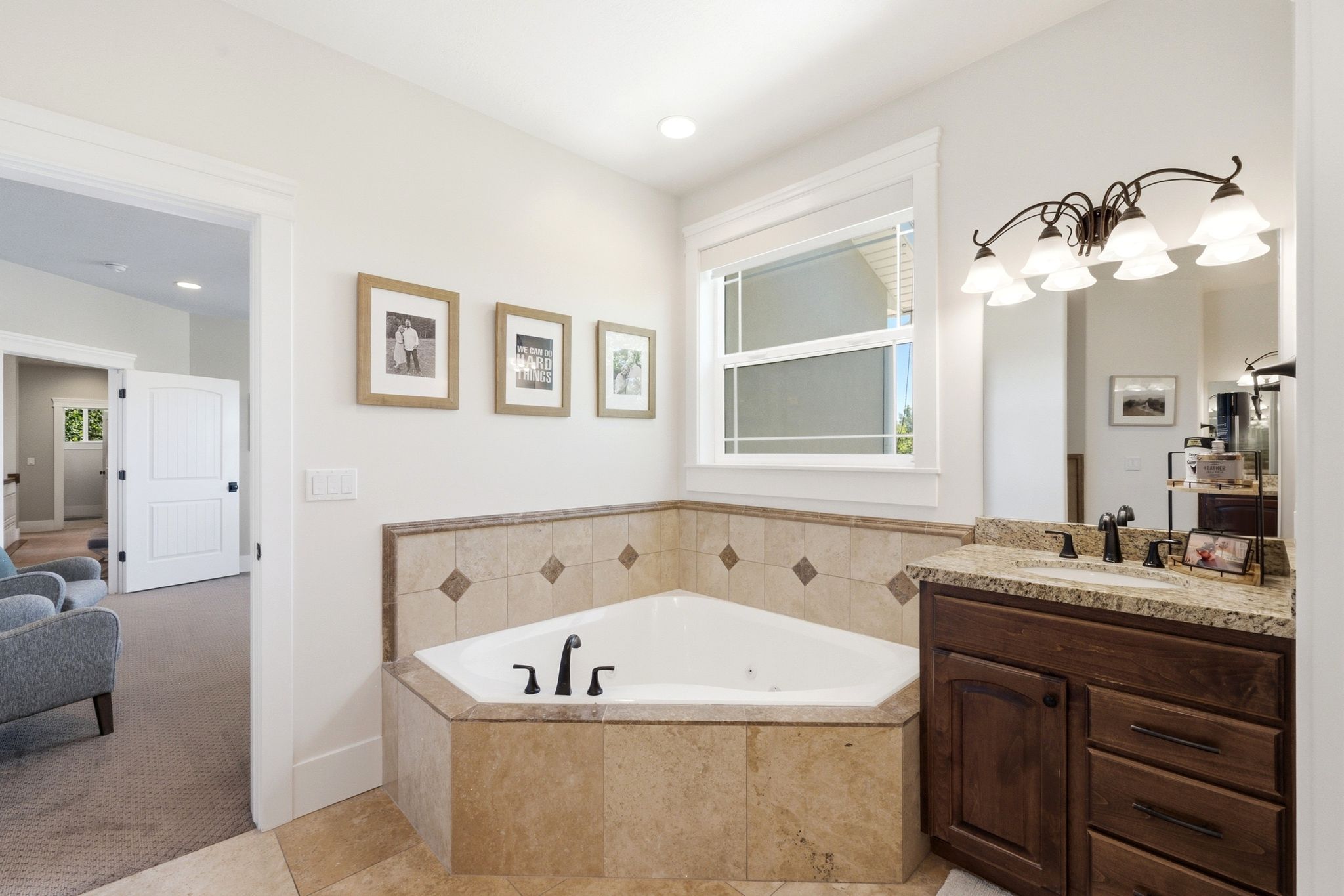 Corner soaking tub with tiled surround, wood-finish vanity with stone-finish countertop, undermount sink, and bronze-finish fixtures