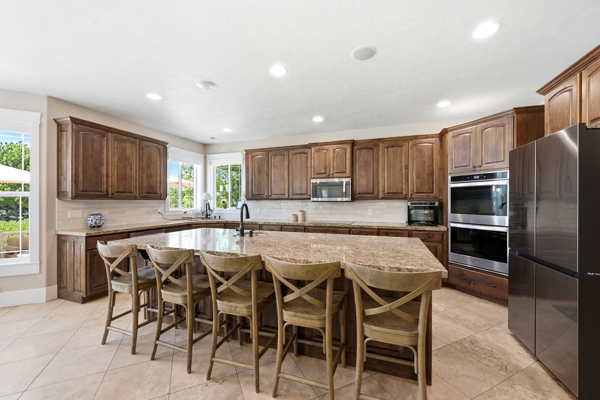 Spacious kitchen featuring a large island with seating, extensive wood cabinetry, light-toned tile flooring, and integrated stainless steel double ovens