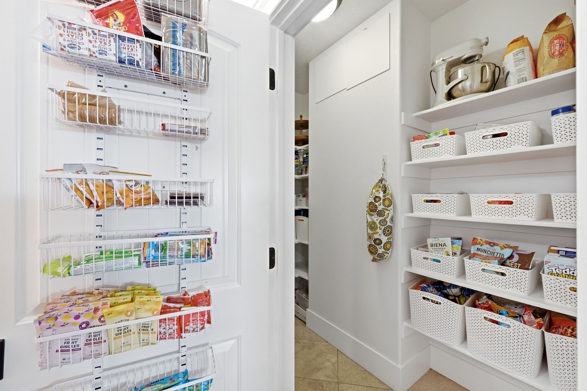 Pantry featuring white built-in shelving, durable tile flooring, and additional door-mounted storage