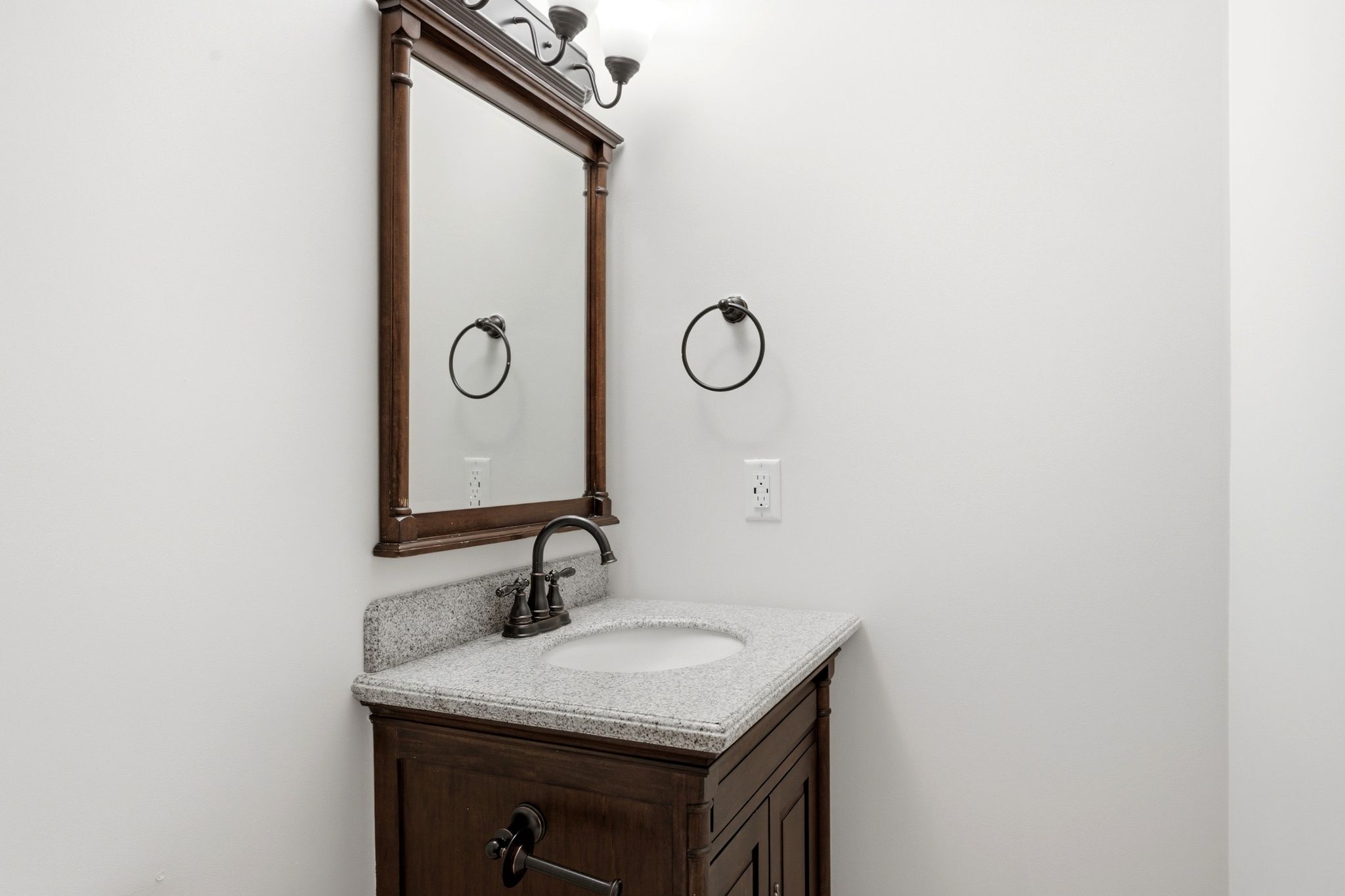 Dark wood-finish vanity with a light speckled countertop, undermount sink, and dark bronze faucet