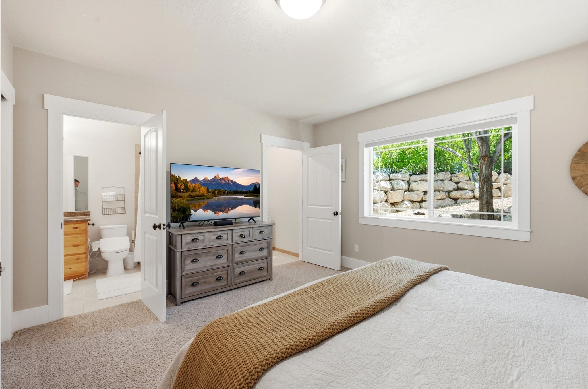 Carpeted bedroom featuring a large window with white trim, a solid white door, and an entryway to an attached bathroom
