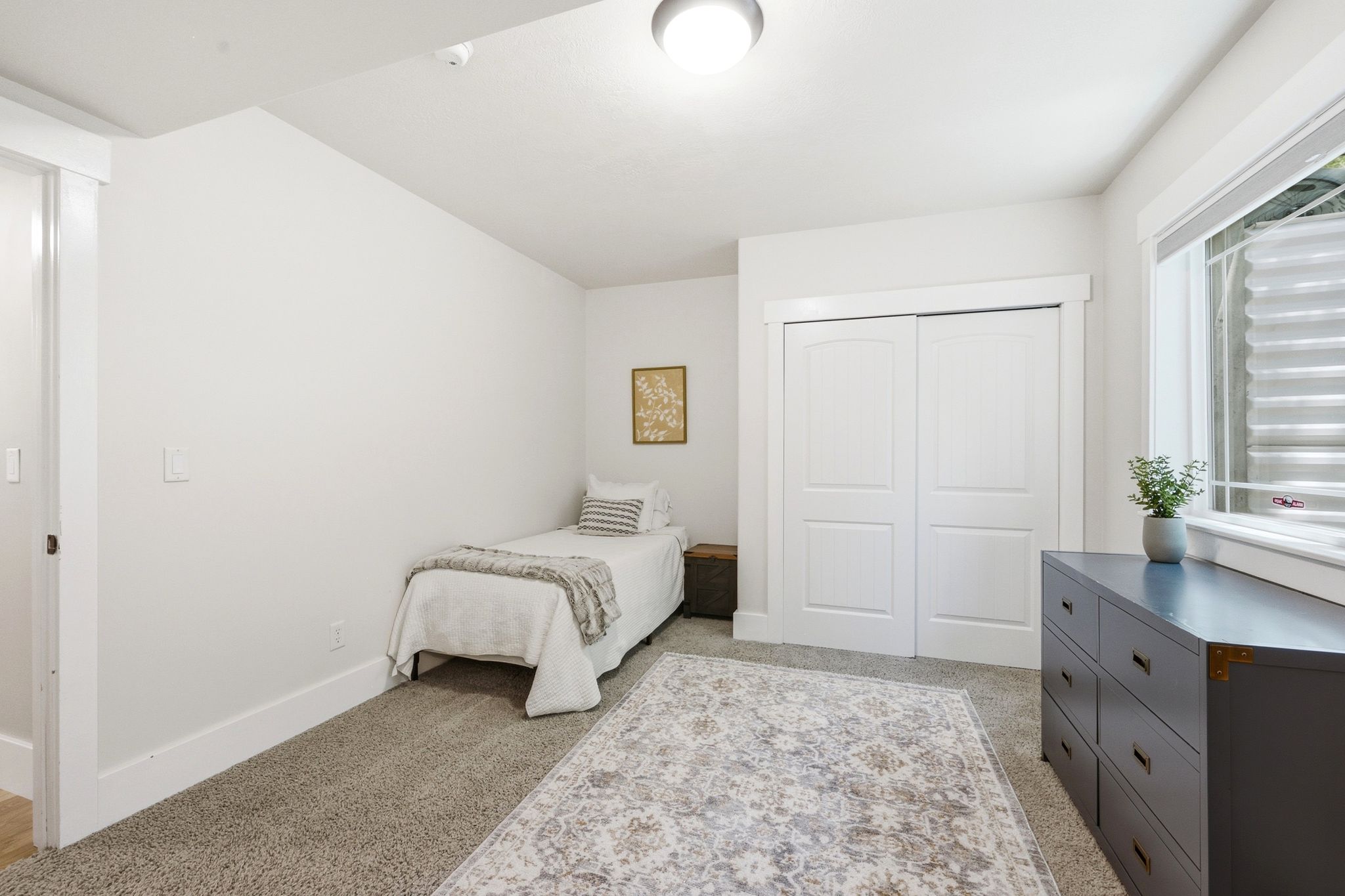 Carpeted room featuring a window with a window blind, a ceiling-mounted light fixture, white trim, and a double-door closet with arch paneling