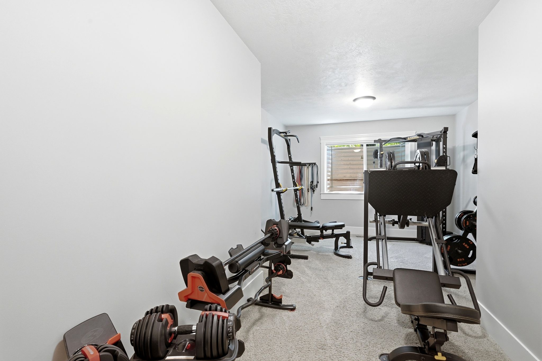 Dedicated exercise space featuring light gray walls, a textured ceiling, a flush-mount ceiling light, and a horizontal window providing natural light