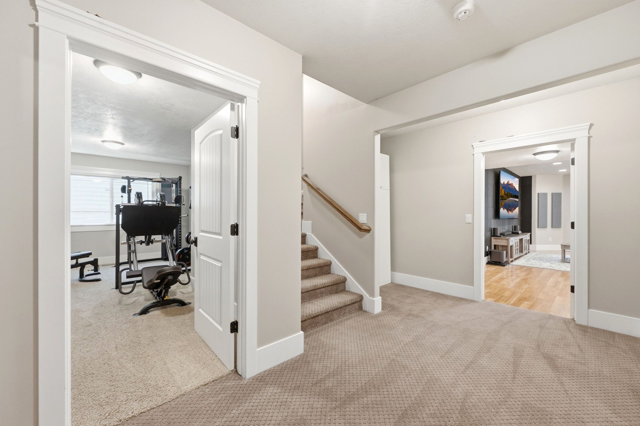 Carpeted hallway featuring a staircase with wood railing, leading to two distinct rooms