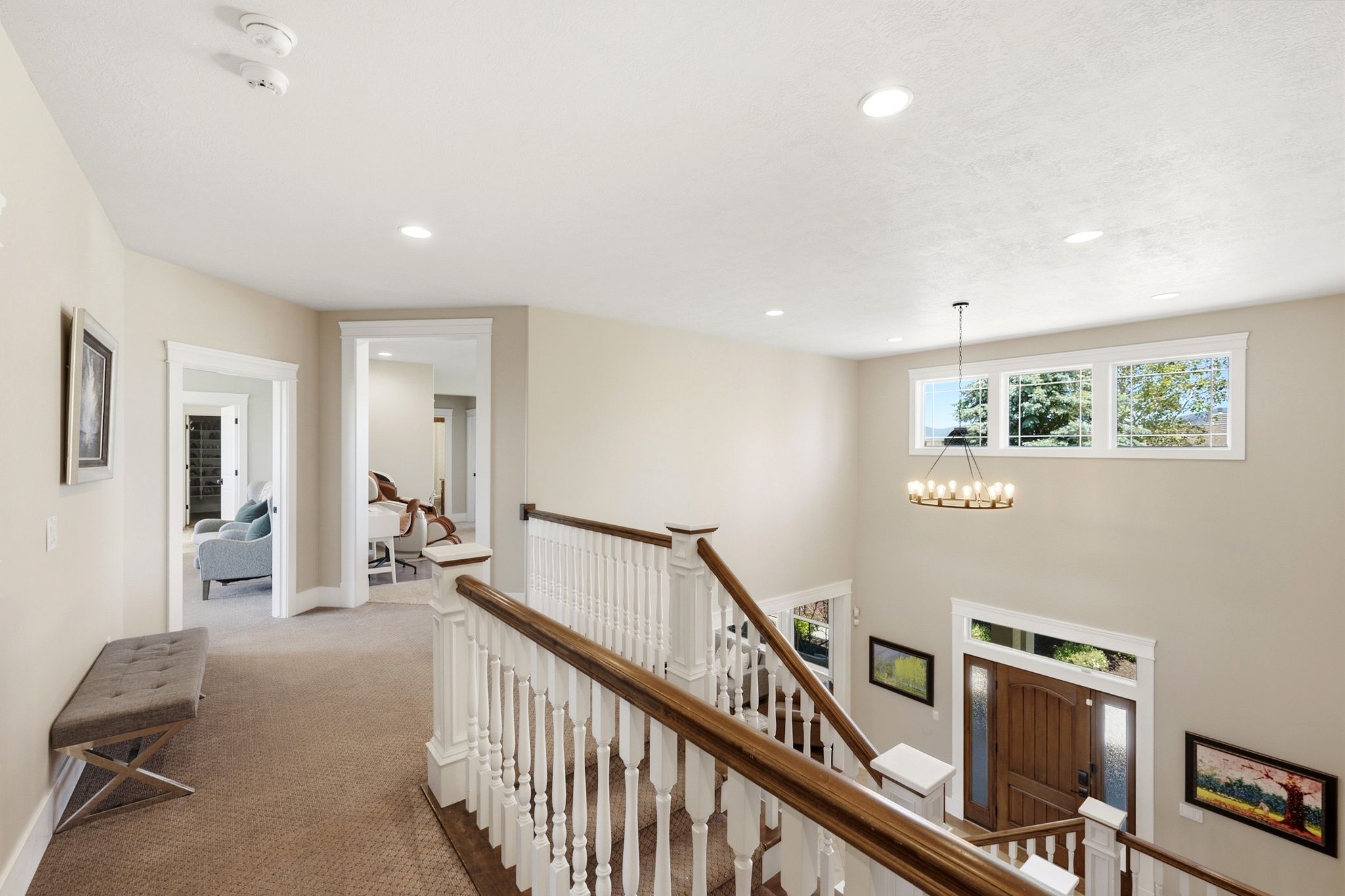 Upper-level landing featuring a wood-finish handrail, white balusters, recessed ceiling lighting, and a chandelier