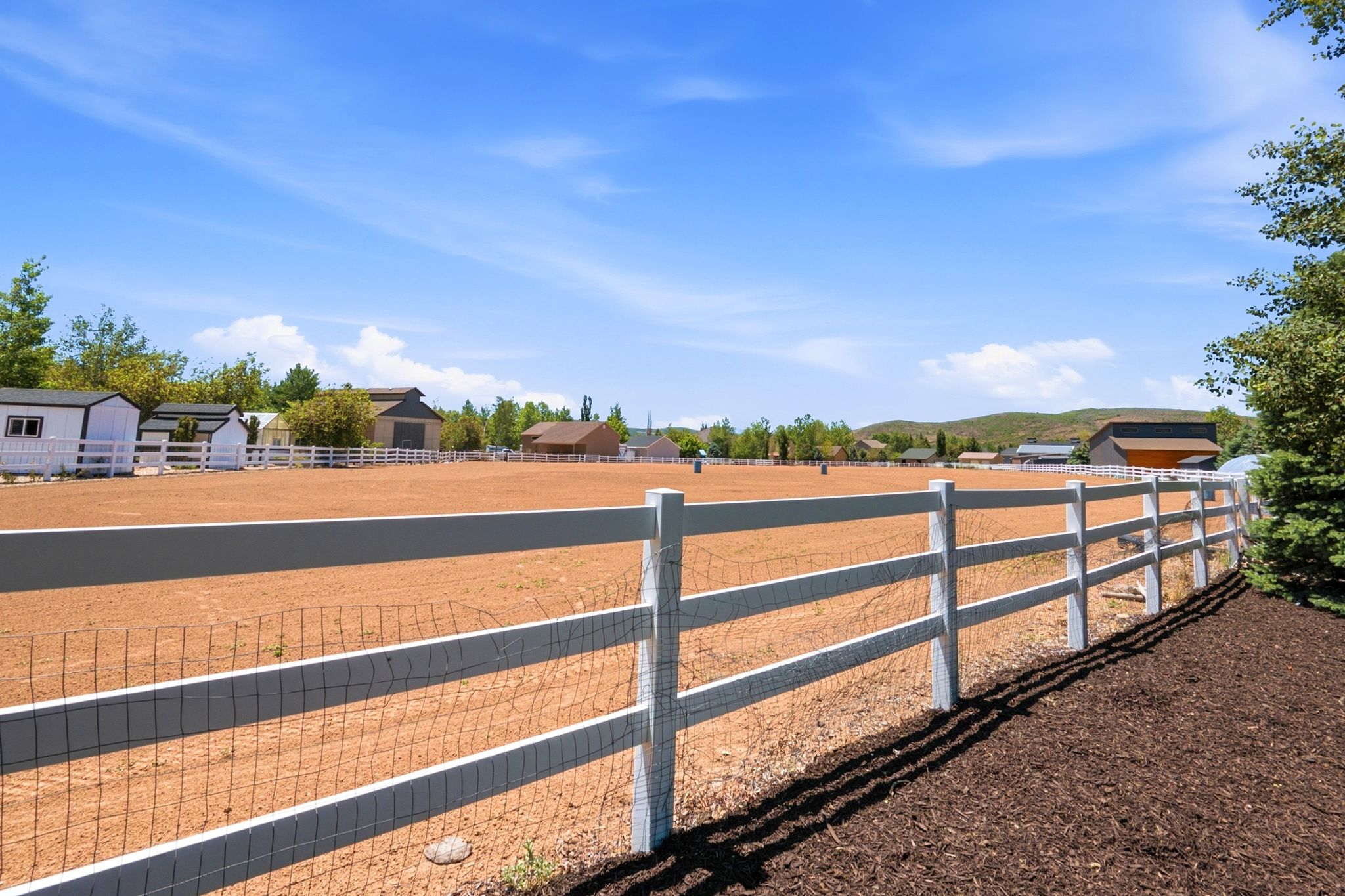 Expansive equestrian arena featuring a white post-and-rail fence with wire mesh