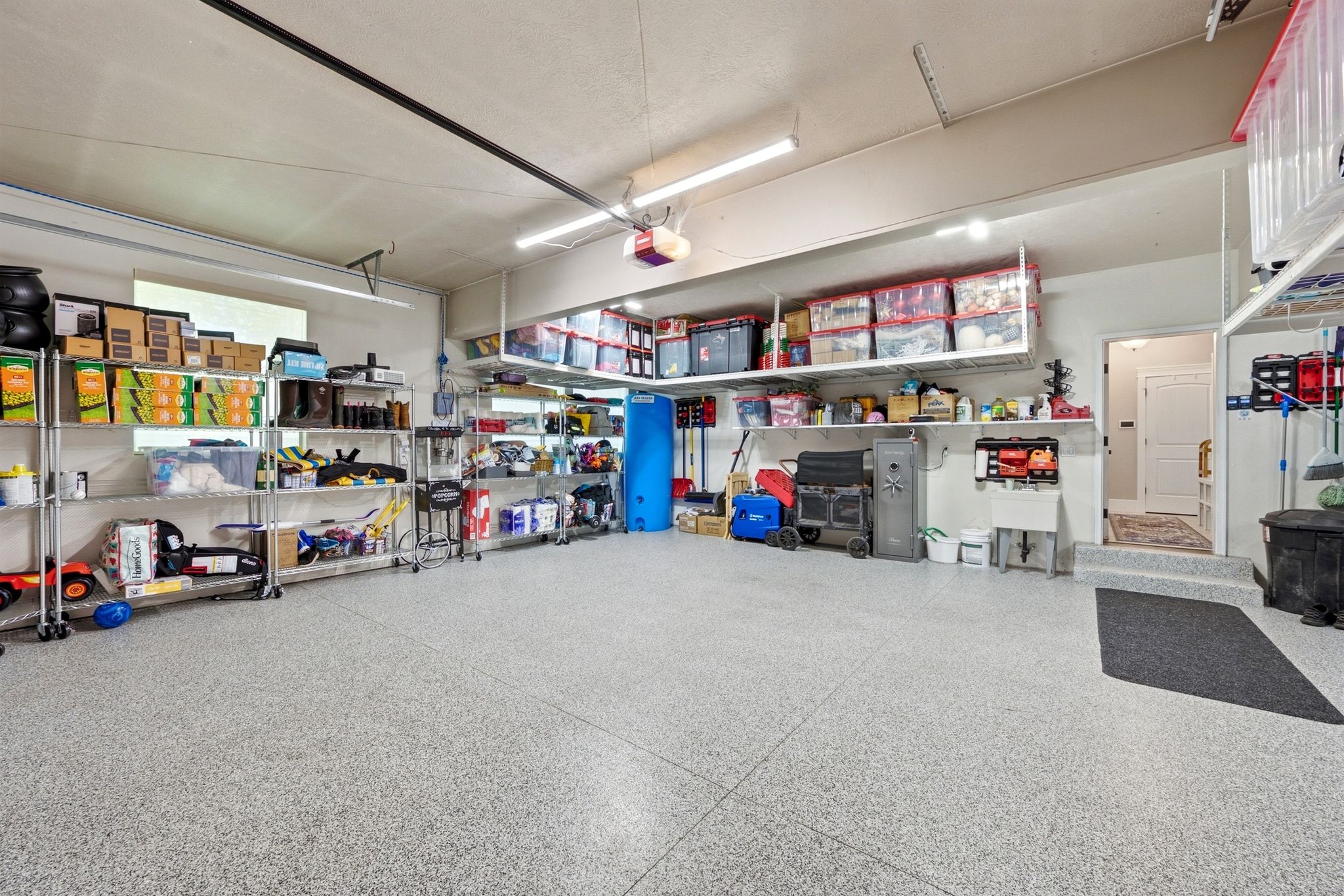 Spacious garage featuring a durable epoxy-coated floor, extensive overhead storage shelving, and additional wall-mounted storage solutions