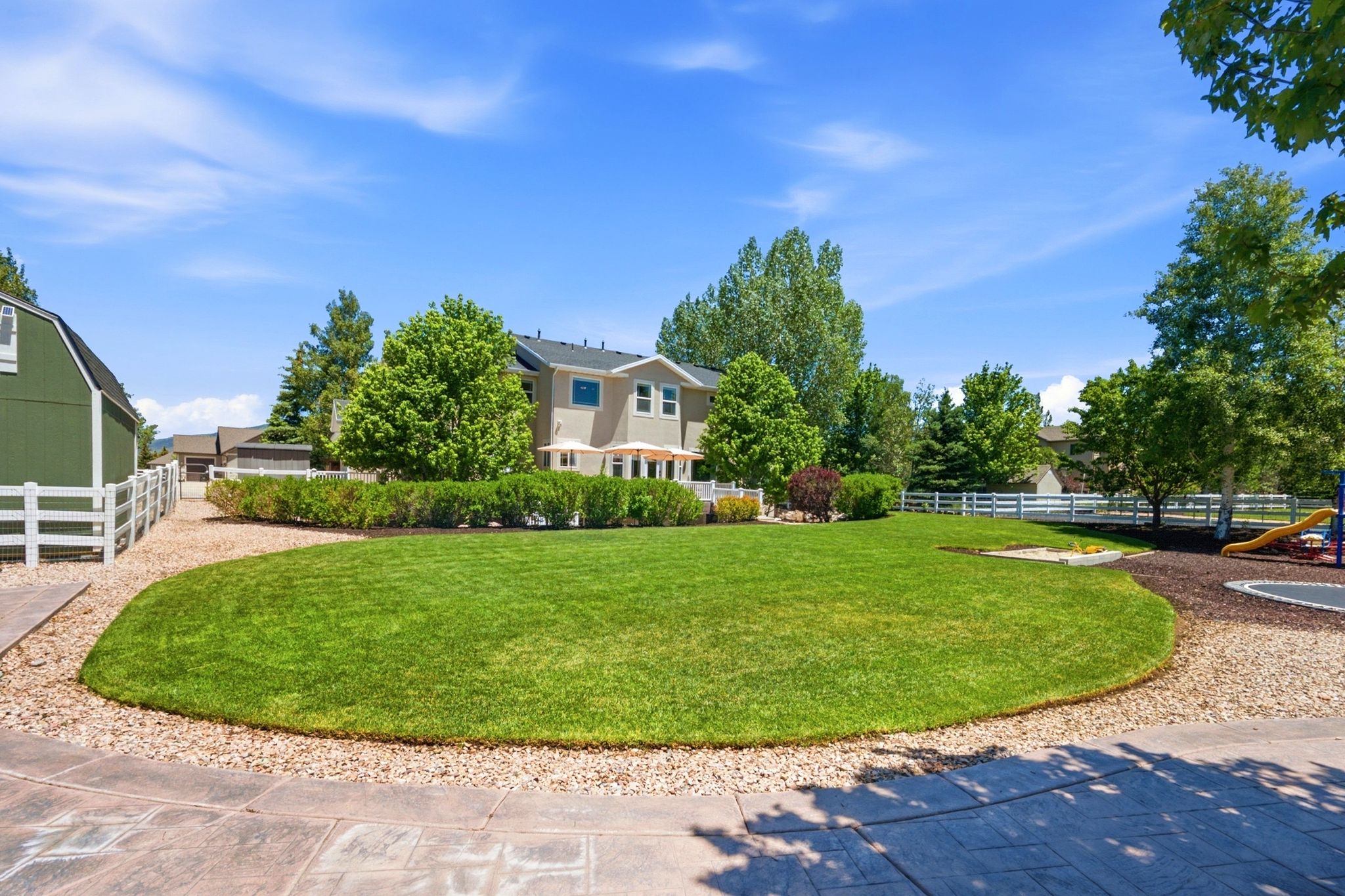 Expansive green lawn surrounded by mature trees and white picket fencing