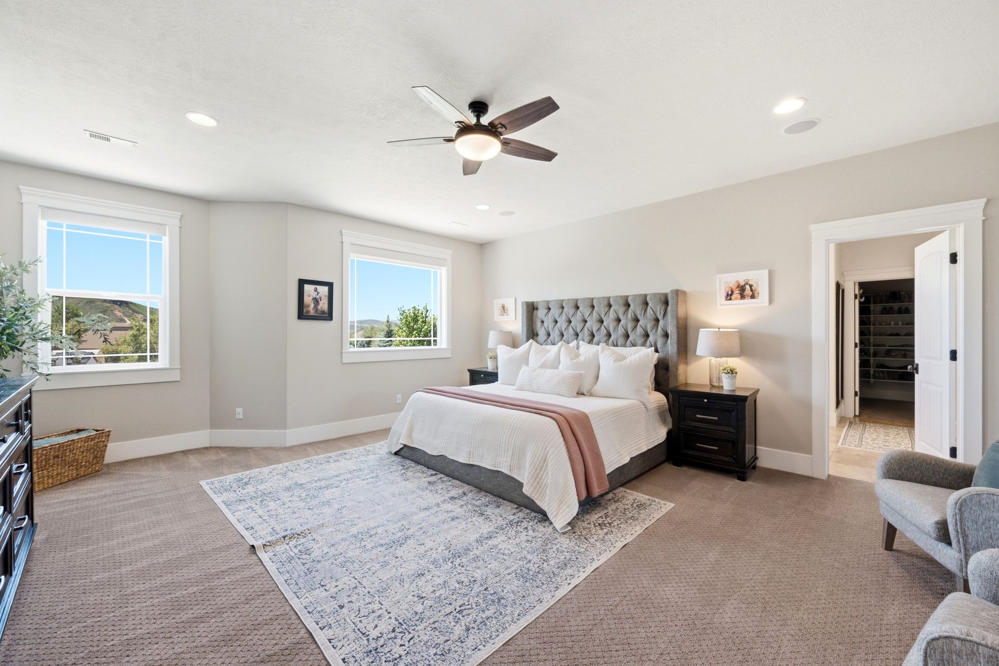 Spacious bedroom featuring neutral carpeting, a ceiling fan, recessed lighting, and two large windows with white trim