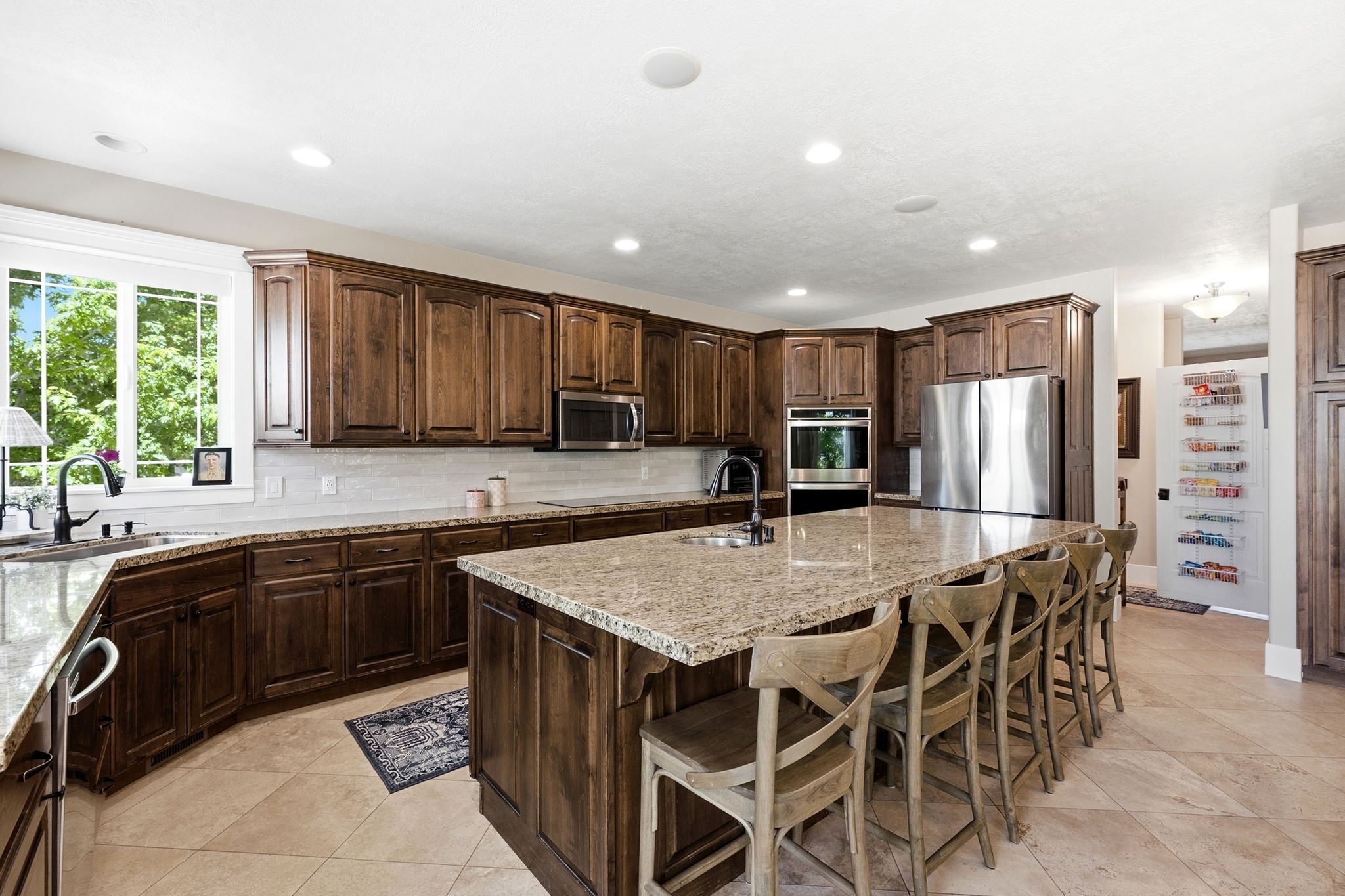Spacious kitchen featuring an oversized island with seating, extensive wood cabinetry, light-toned stone countertops, and stainless steel appliances, all complemented by large format floor tiles