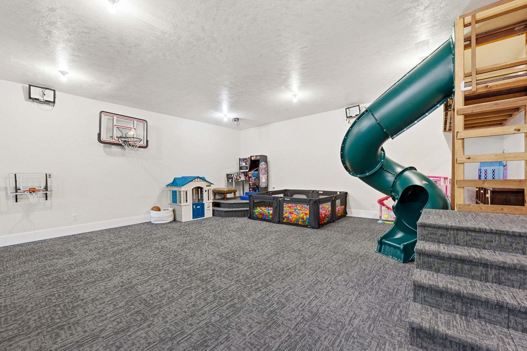 Lower level recreation space featuring a built-in play structure with an enclosed slide, dedicated carpeted stairs, and recessed lighting