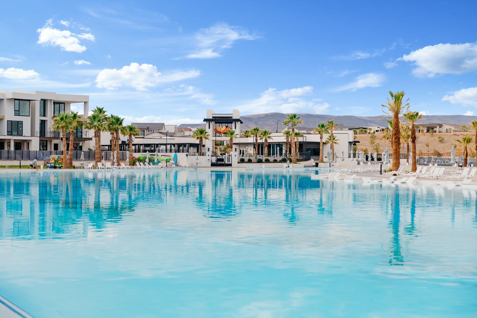 Expansive blue lagoon bordered by modern architecture, palm trees, and a sun shelf with lounge seating
