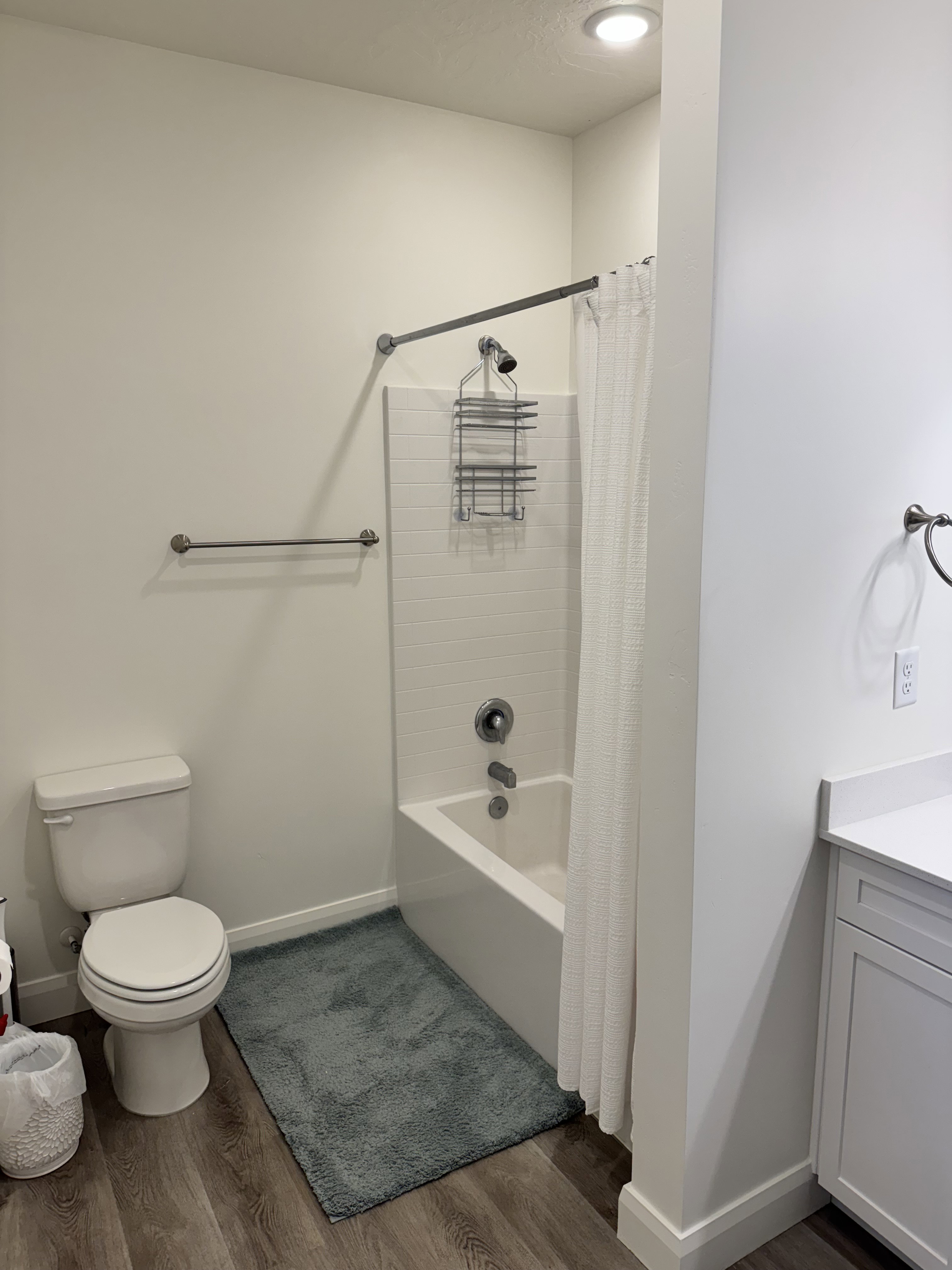 Bathroom featuring a white tub/shower combination with subway tile surround, a toilet, and wood-finish flooring