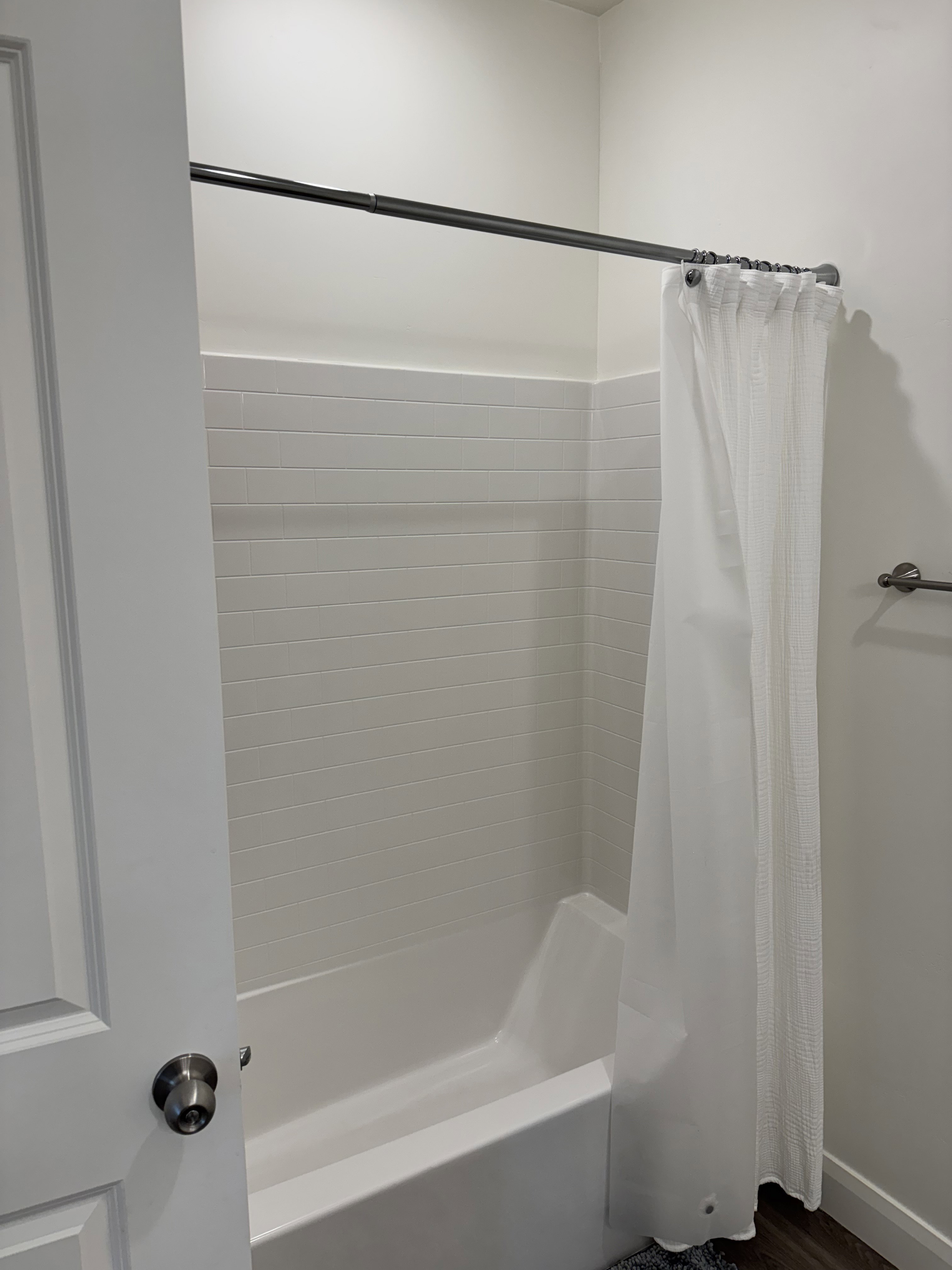 Shower-tub combination with white subway tile surround and dark wood-finish flooring