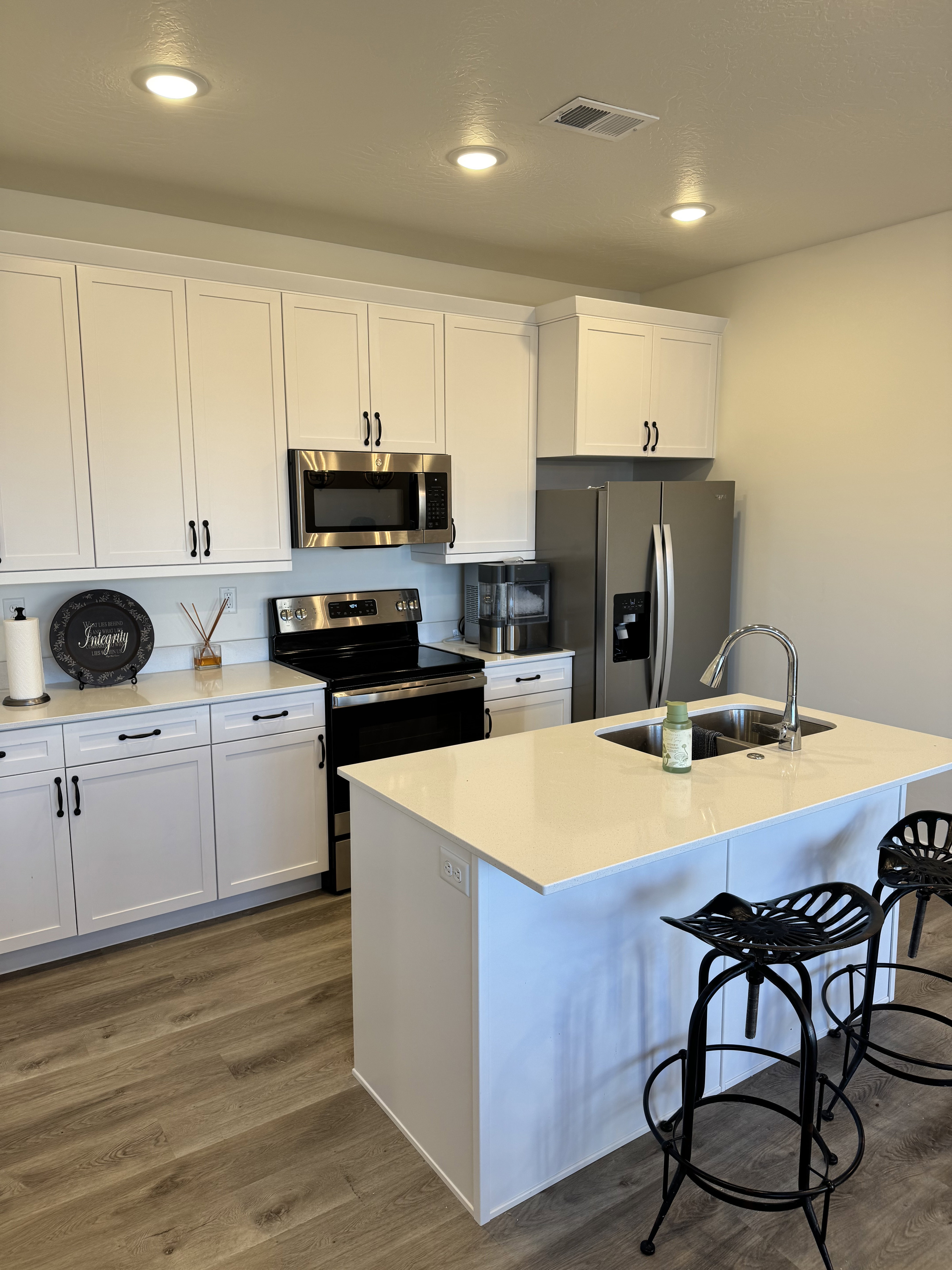 Contemporary kitchen featuring white cabinetry, stainless steel appliances, light-toned countertops, a central island with an undermount double sink, and wood-finish flooring
