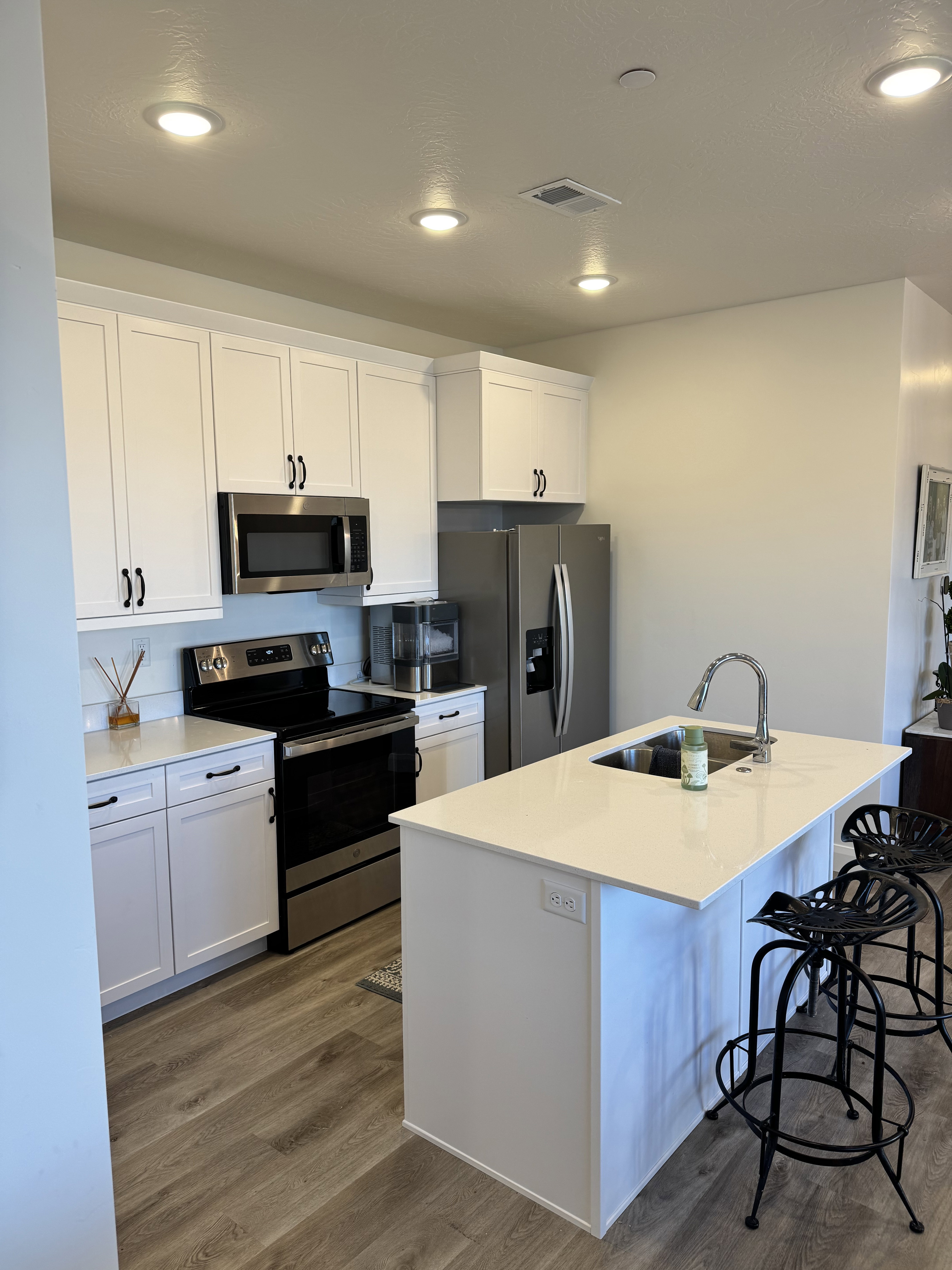 Contemporary kitchen featuring white cabinetry, stainless steel appliances, wood-finish flooring, recessed lighting, and a center island with sink