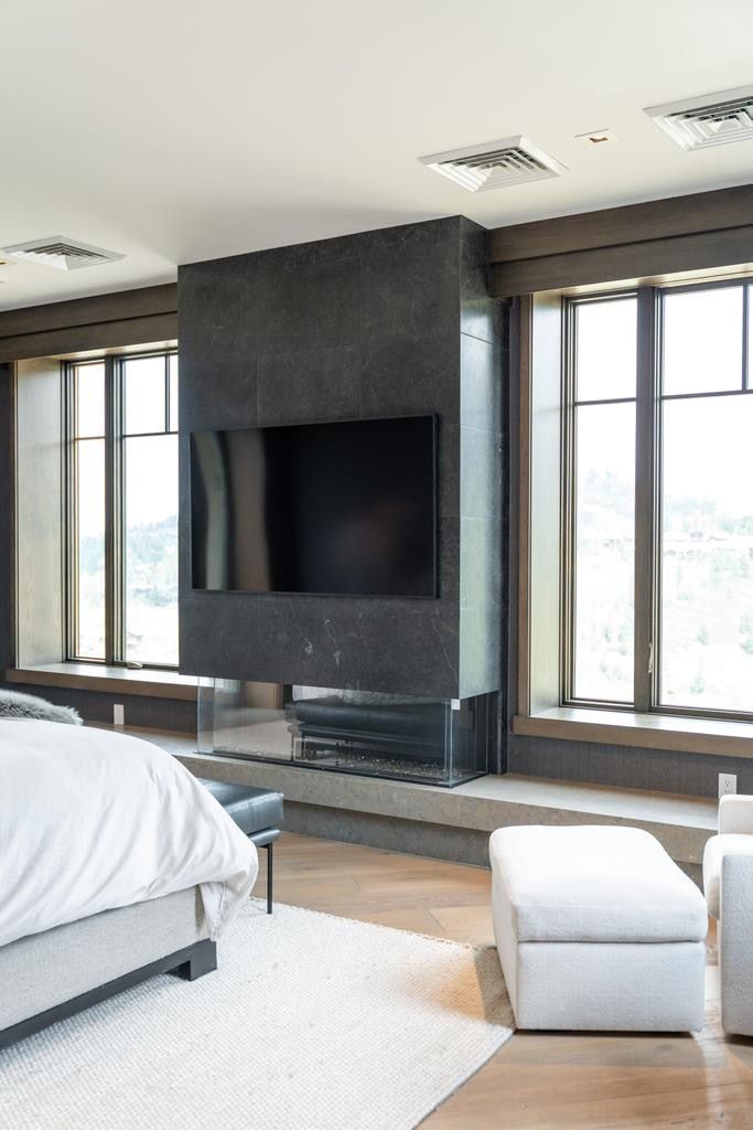 Modern fireplace feature with a glass-enclosed firebox, integrated television, and dark stone surround