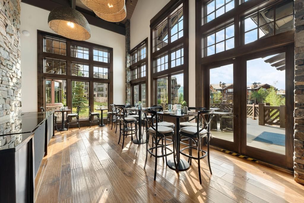 Spacious interior featuring expansive floor-to-ceiling windows with dark wood framing, rich wood-finish flooring, and a stone accent wall