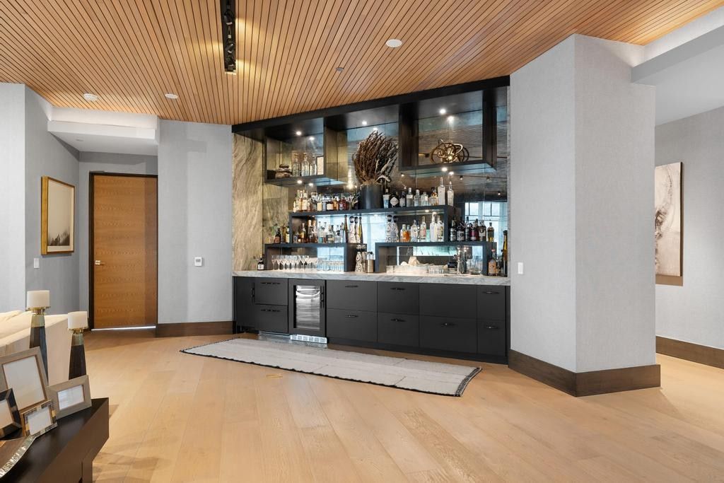 Integrated wet bar featuring black cabinetry, light stone countertop, mirrored backsplash, and built-in beverage cooler