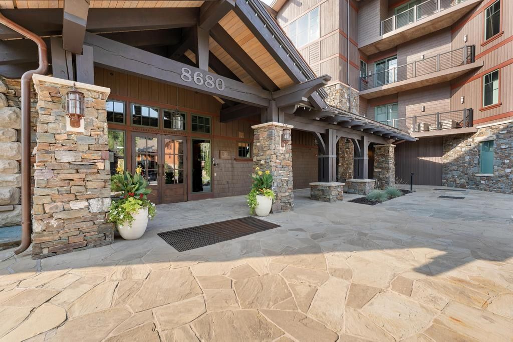 Rustic-inspired building exterior featuring stone cladding, wood siding, a flagstone entryway, exposed wood beams, and a covered portico entrance