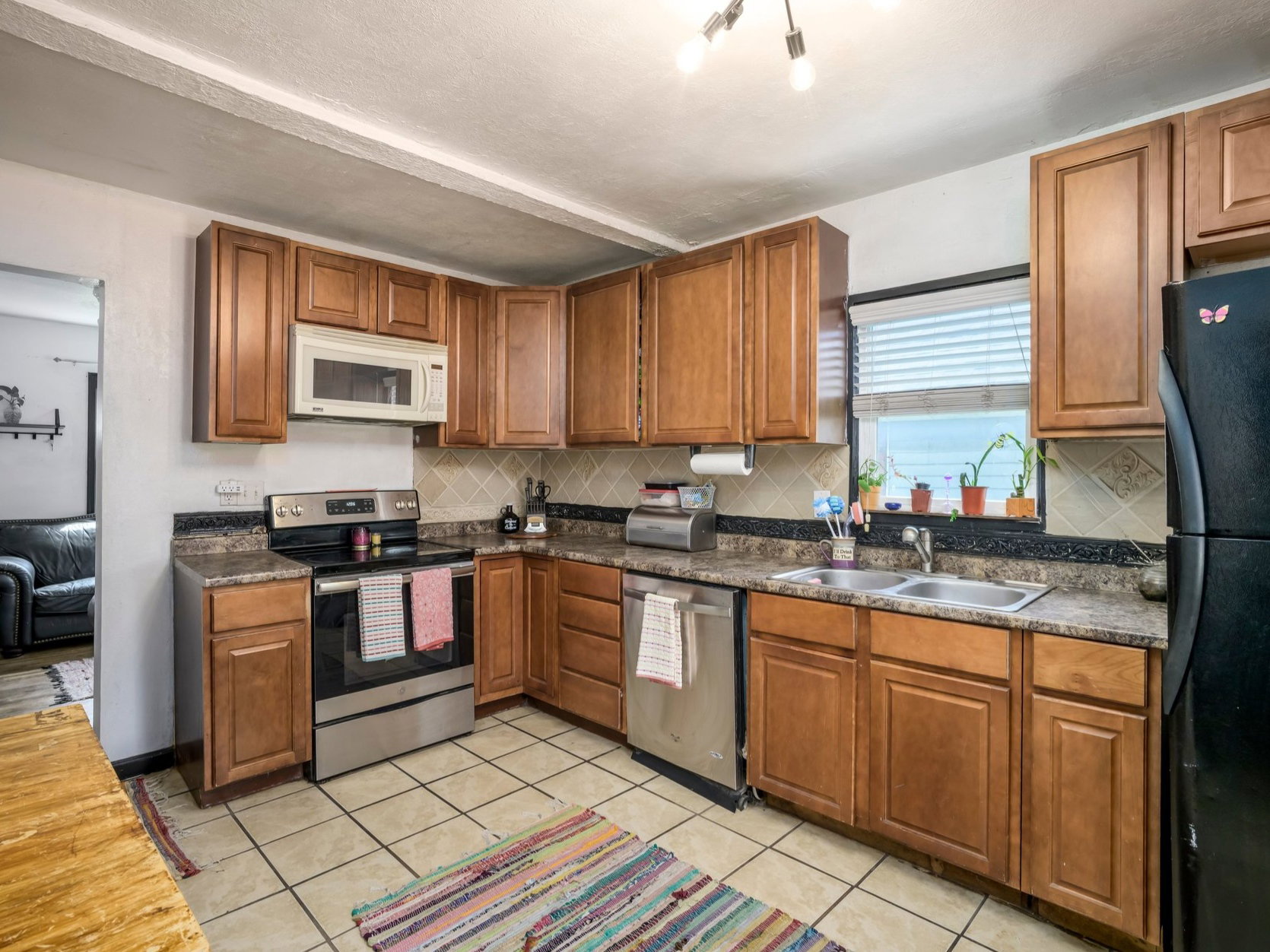 Kitchen featuring wood cabinetry, solid surface countertops, tile flooring, and stainless steel appliances including a range, microwave, and dishwasher