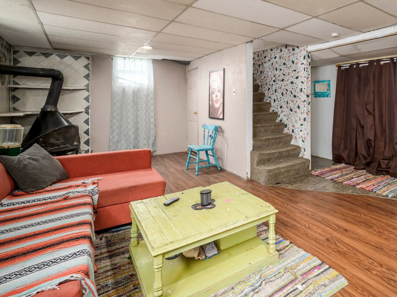 Finished lower level featuring wood-finish flooring, a built-in wood-burning stove with shelving, and concrete stairs