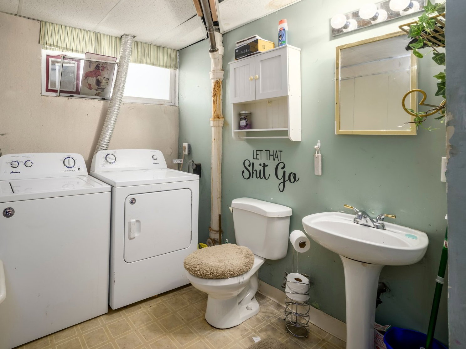 Laundry area with a drop ceiling, pedestal sink, toilet, and exposed piping